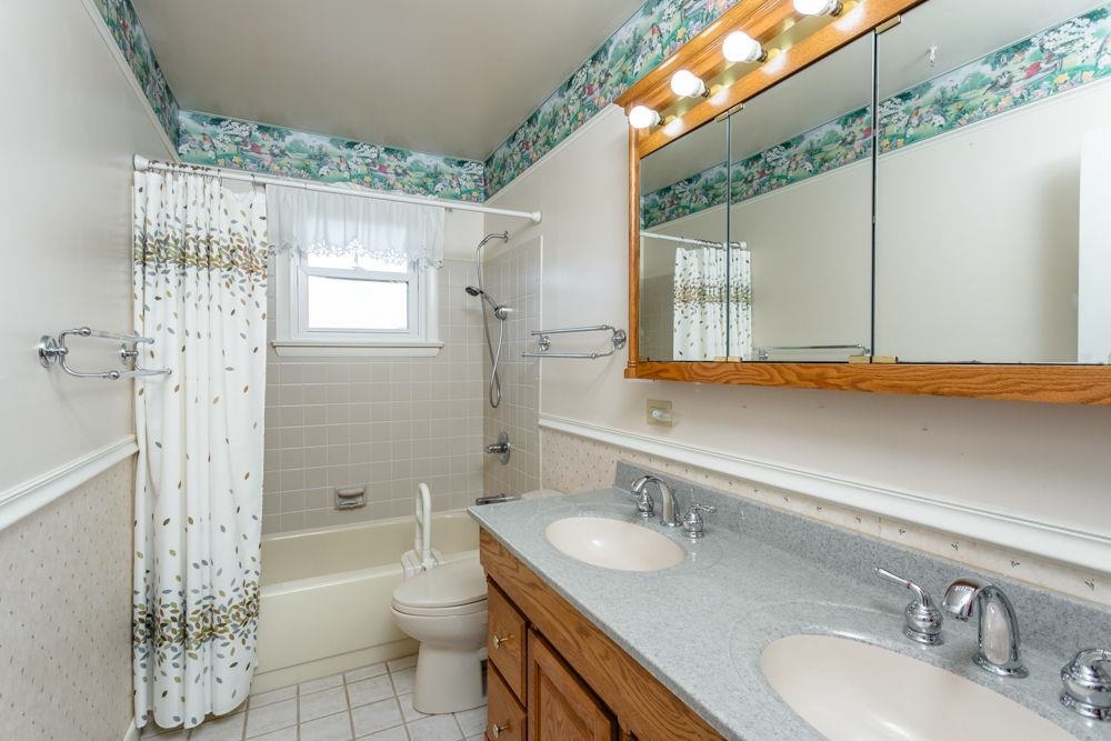 Oak cabinet with dual sinks. Tile wall and floors.