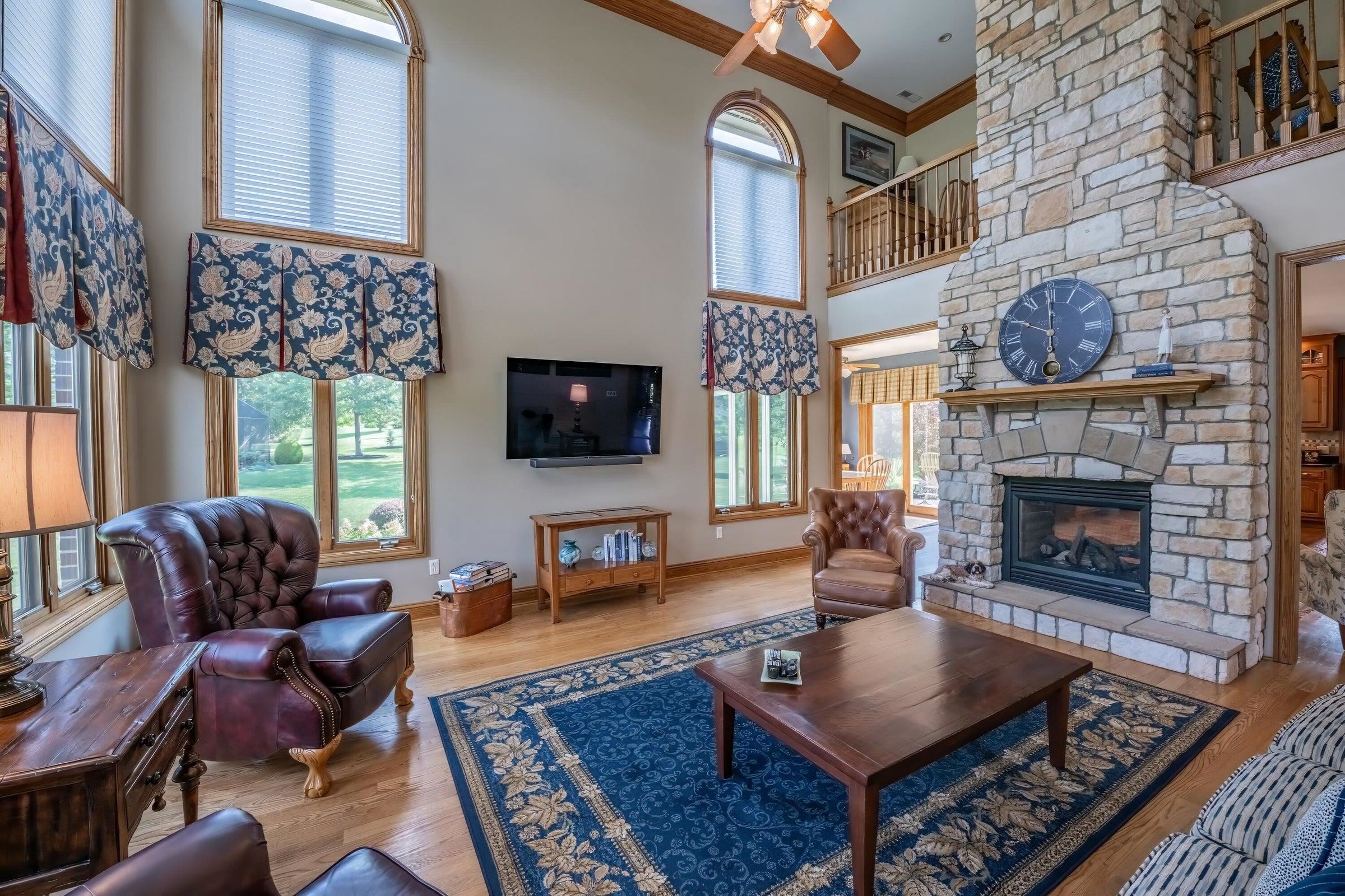 Great Room with stone fireplace, oak floors, and 2-story windows.