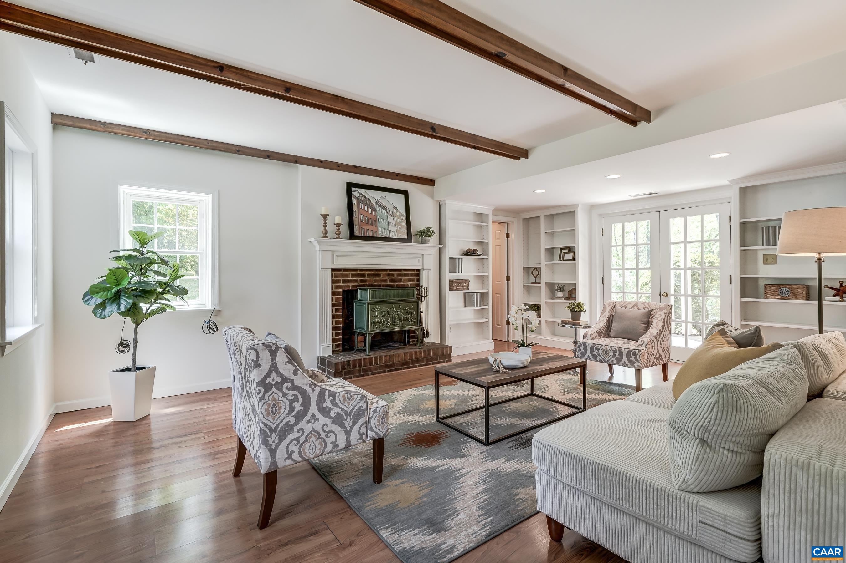 Cozy living room features exposed beams, built in shelves, and brick fireplace with woodstove.