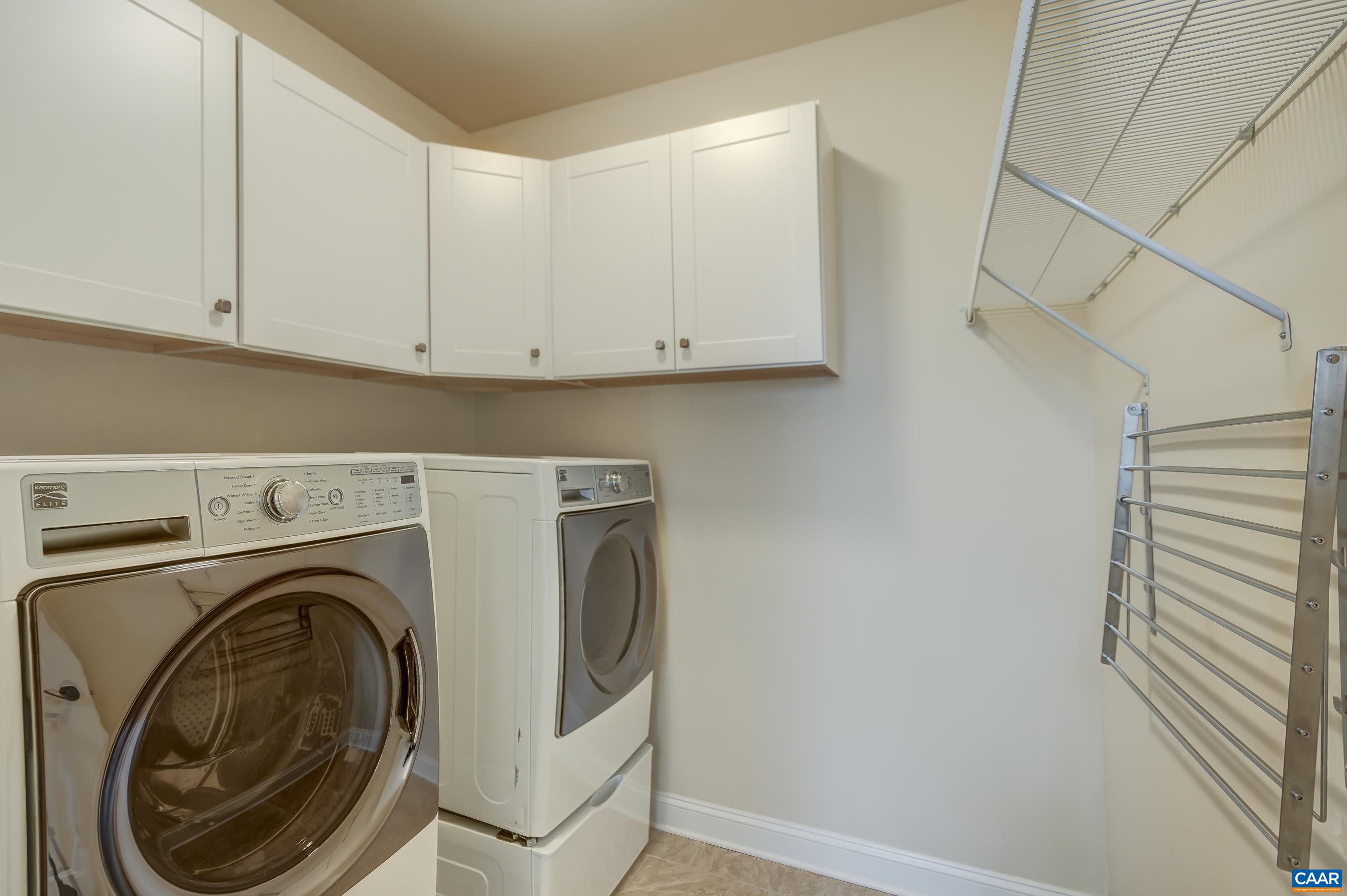 Main level laundry room with pedestal washer and dryer, storage cabinets and drying rack.