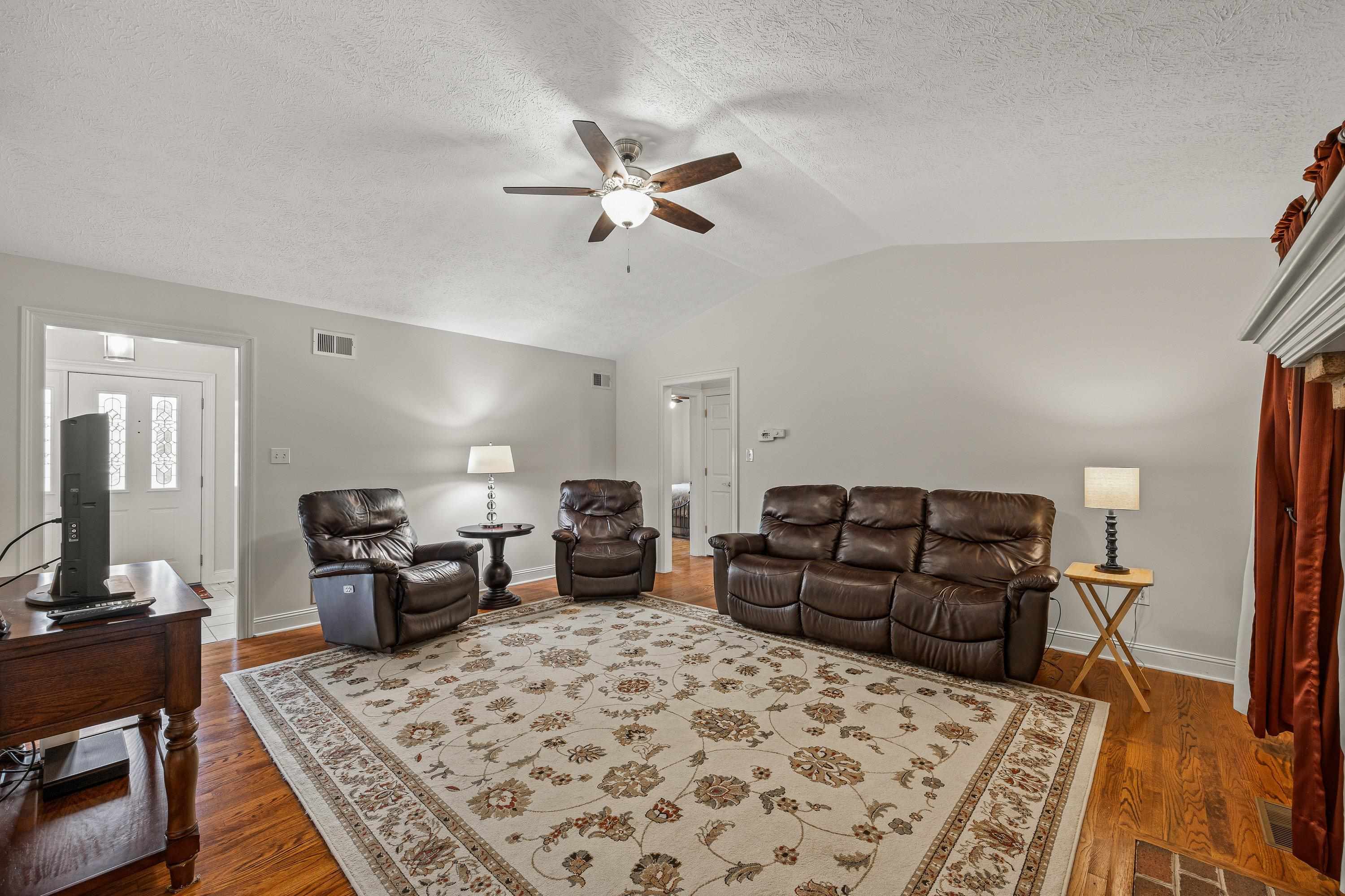 Open and bright, this living room space contains a brick wood fireplace, hardwood flooring, large windows, ceiling fan, and an abundance of space for gathering with family and friends!