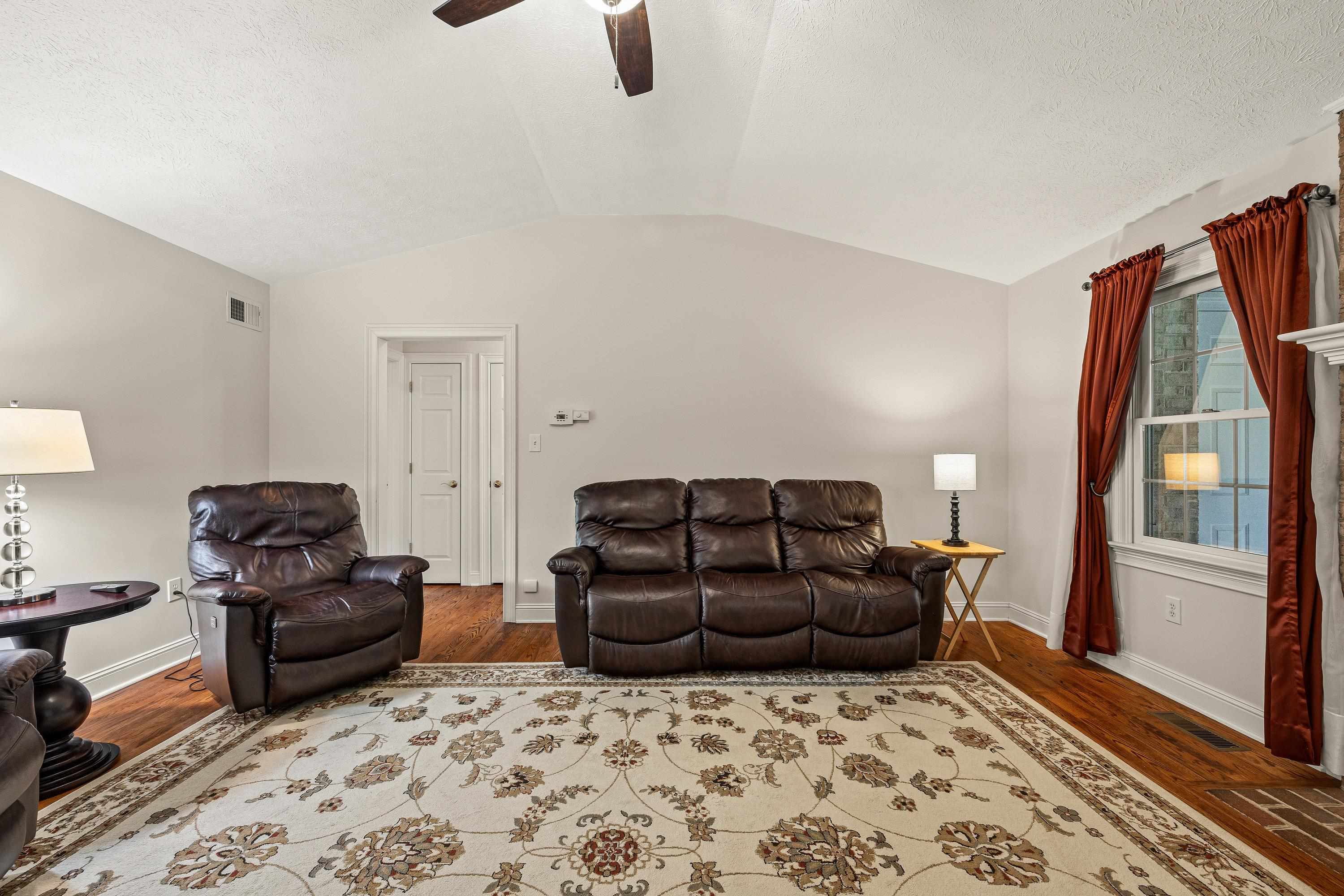 Open and bright, this living room space contains a brick wood fireplace, hardwood flooring, large windows, ceiling fan, and an abundance of space for gathering with family and friends!