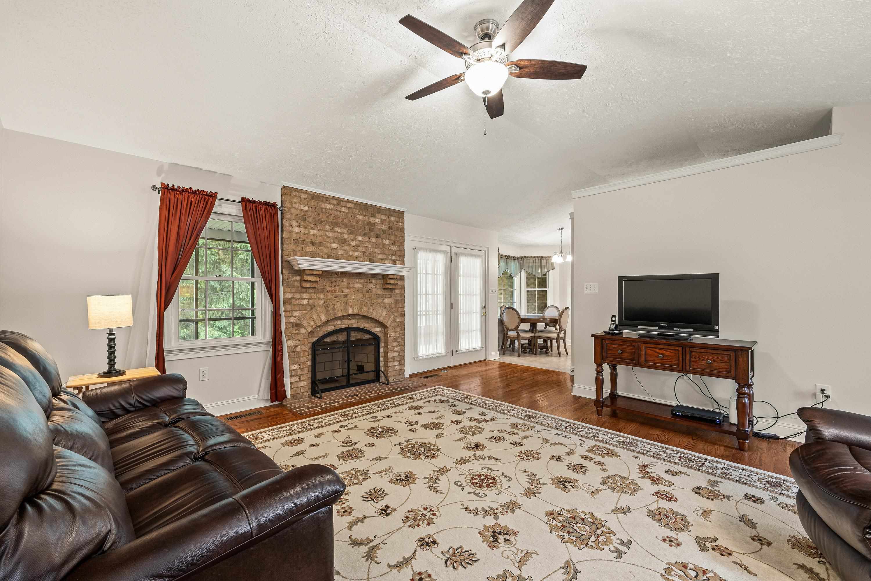 Open and bright, this living room space contains a brick wood fireplace, hardwood flooring, large windows, ceiling fan, and an abundance of space for gathering with family and friends!