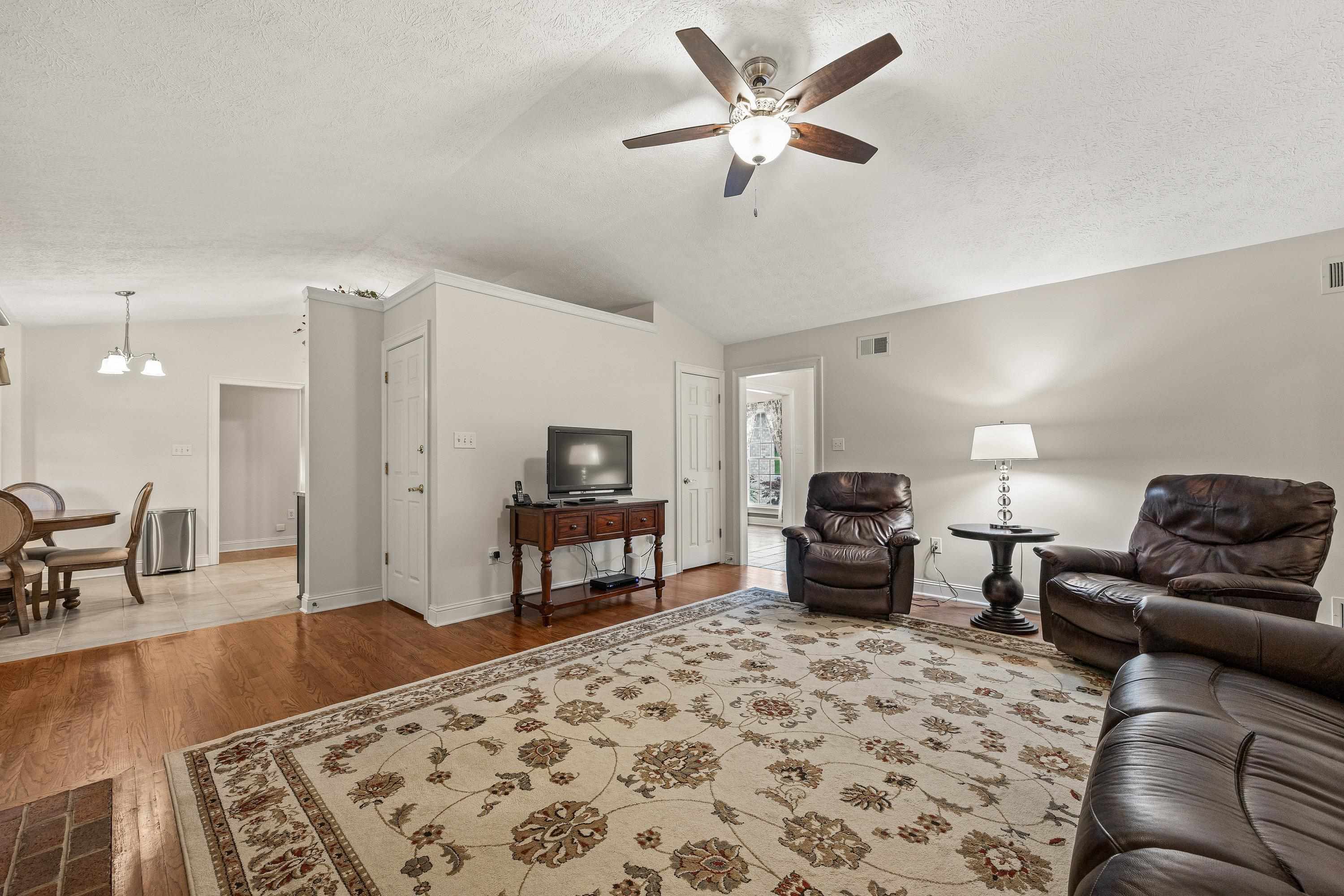 Open and bright, this living room space contains a brick wood fireplace, hardwood flooring, large windows, ceiling fan, and an abundance of space for gathering with family and friends!
