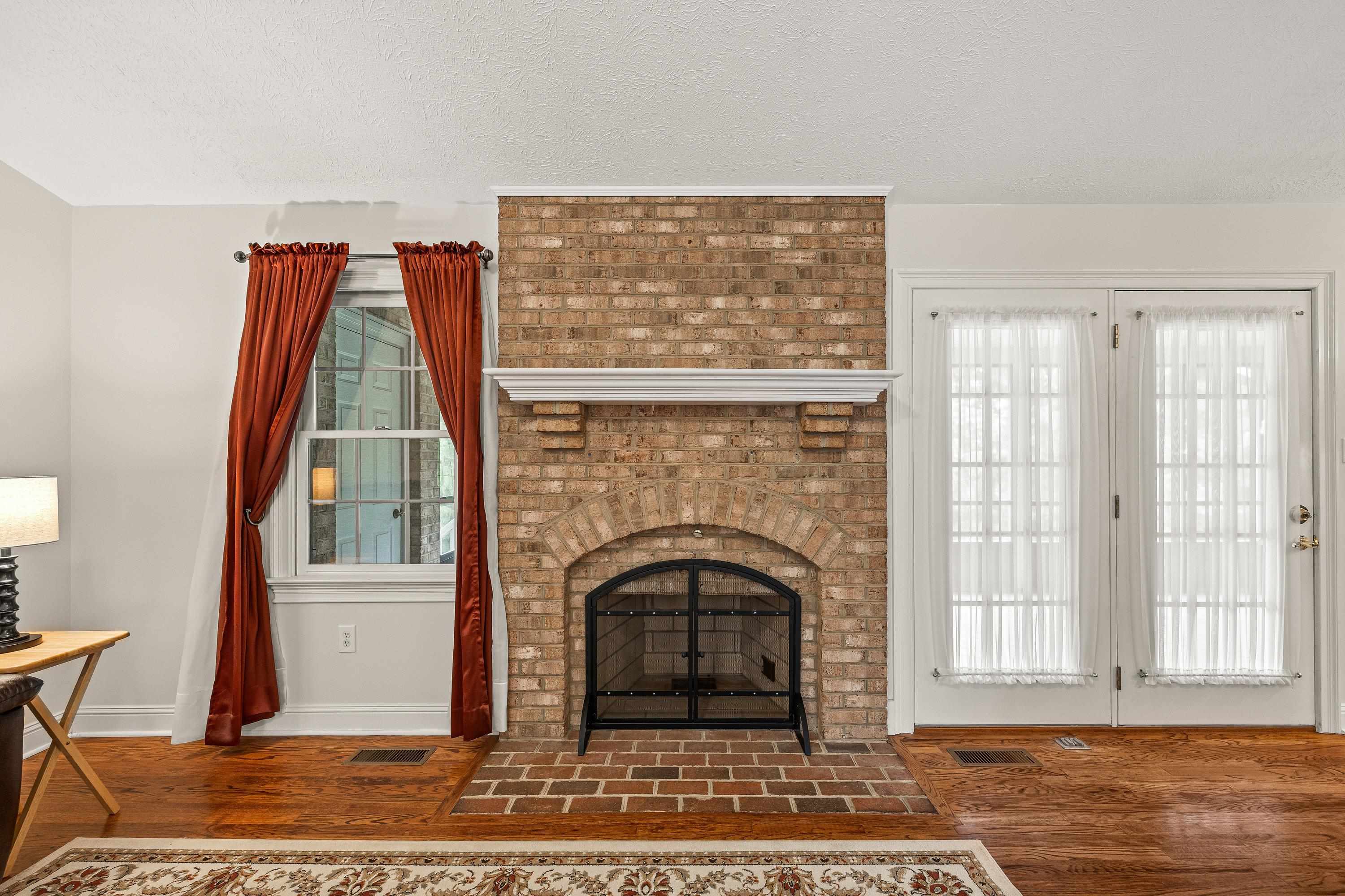 Open and bright, this living room space contains a brick wood fireplace, hardwood flooring, large windows, ceiling fan, and an abundance of space for gathering with family and friends!