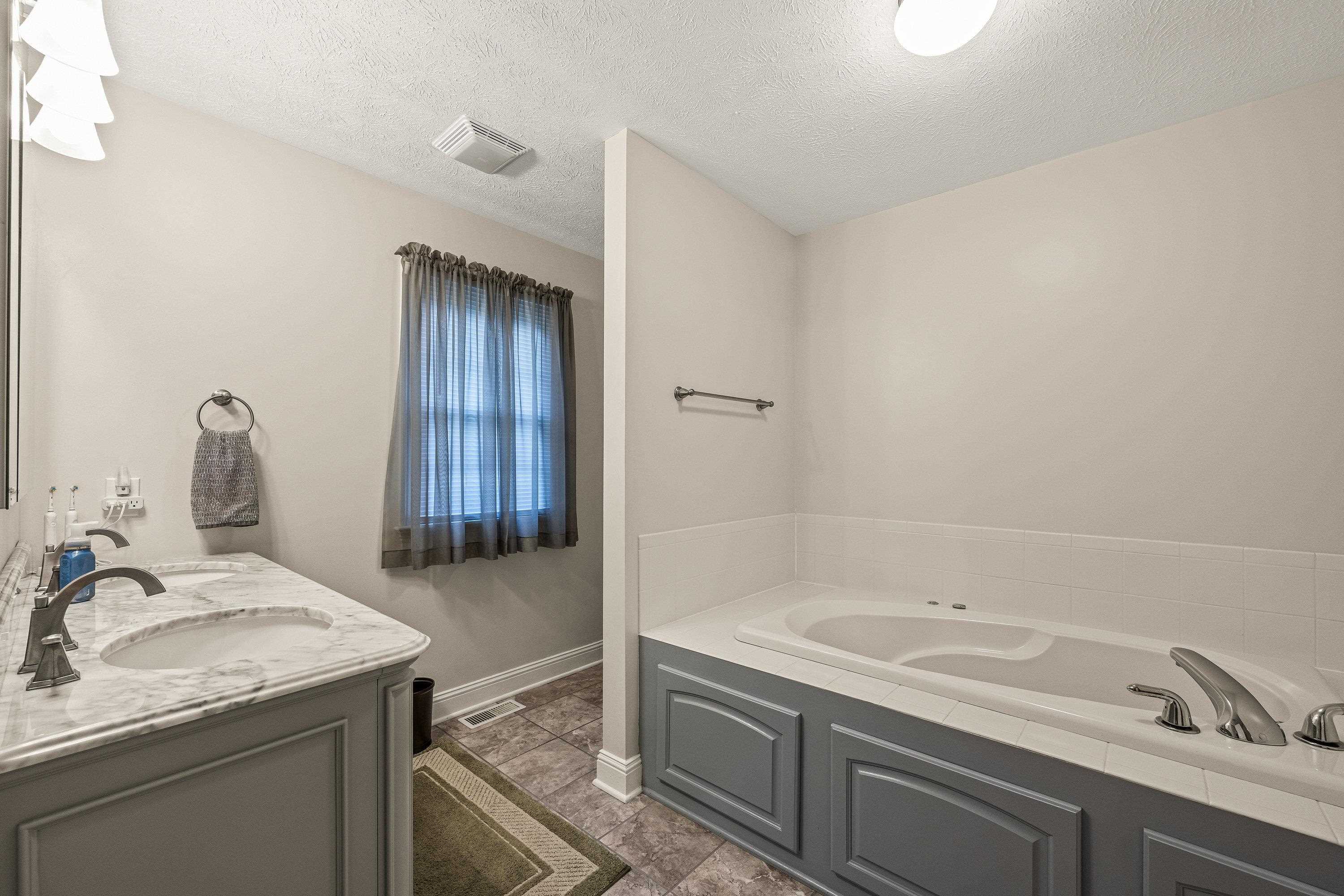 The attached bathroom offers updates throughout.  This space features a whirlpool bathtub, stand-up shower, and dual vanities with storage cabinetry.