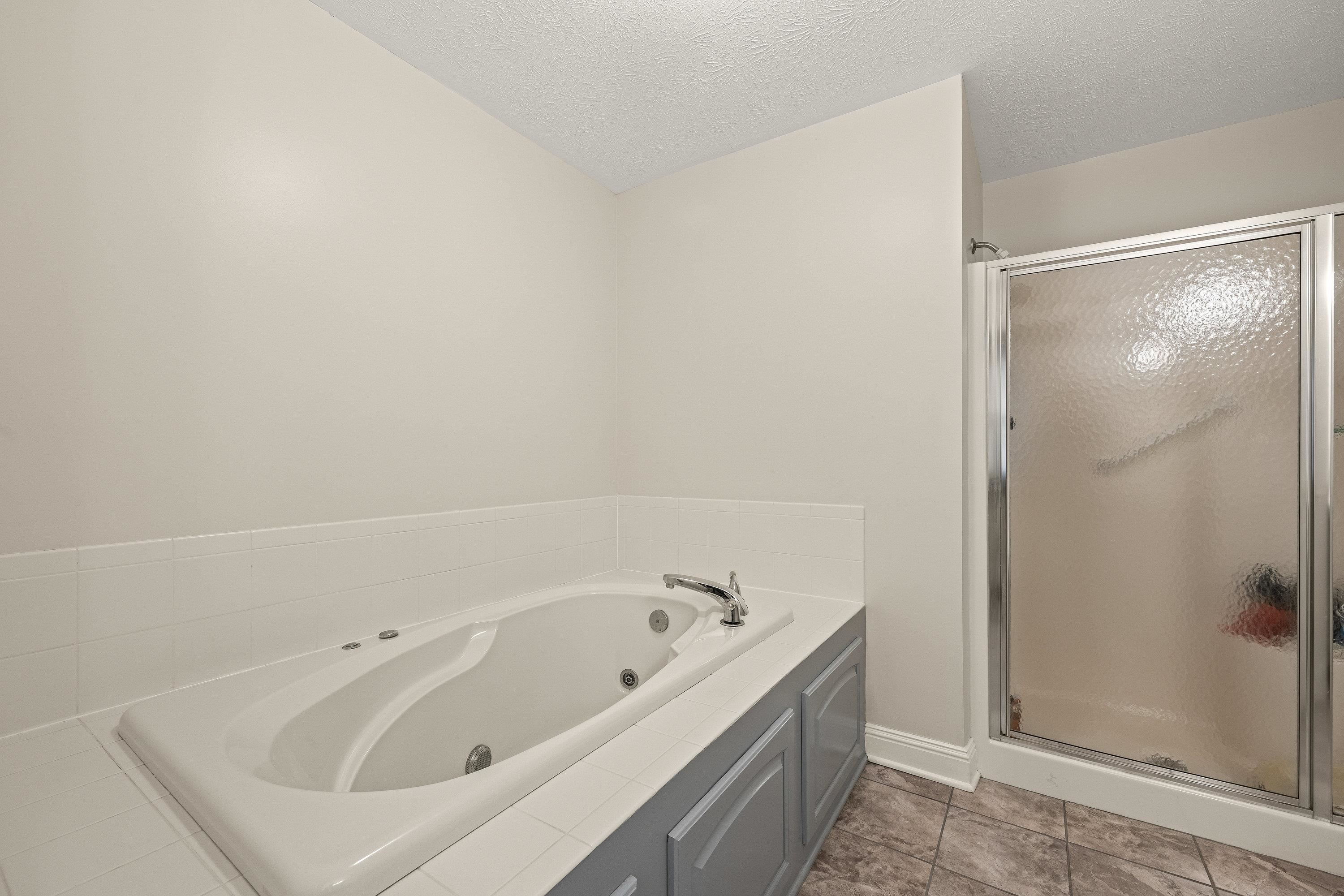 The attached bathroom offers updates throughout.  This space features a whirlpool bathtub, stand-up shower, and dual vanities with storage cabinetry.