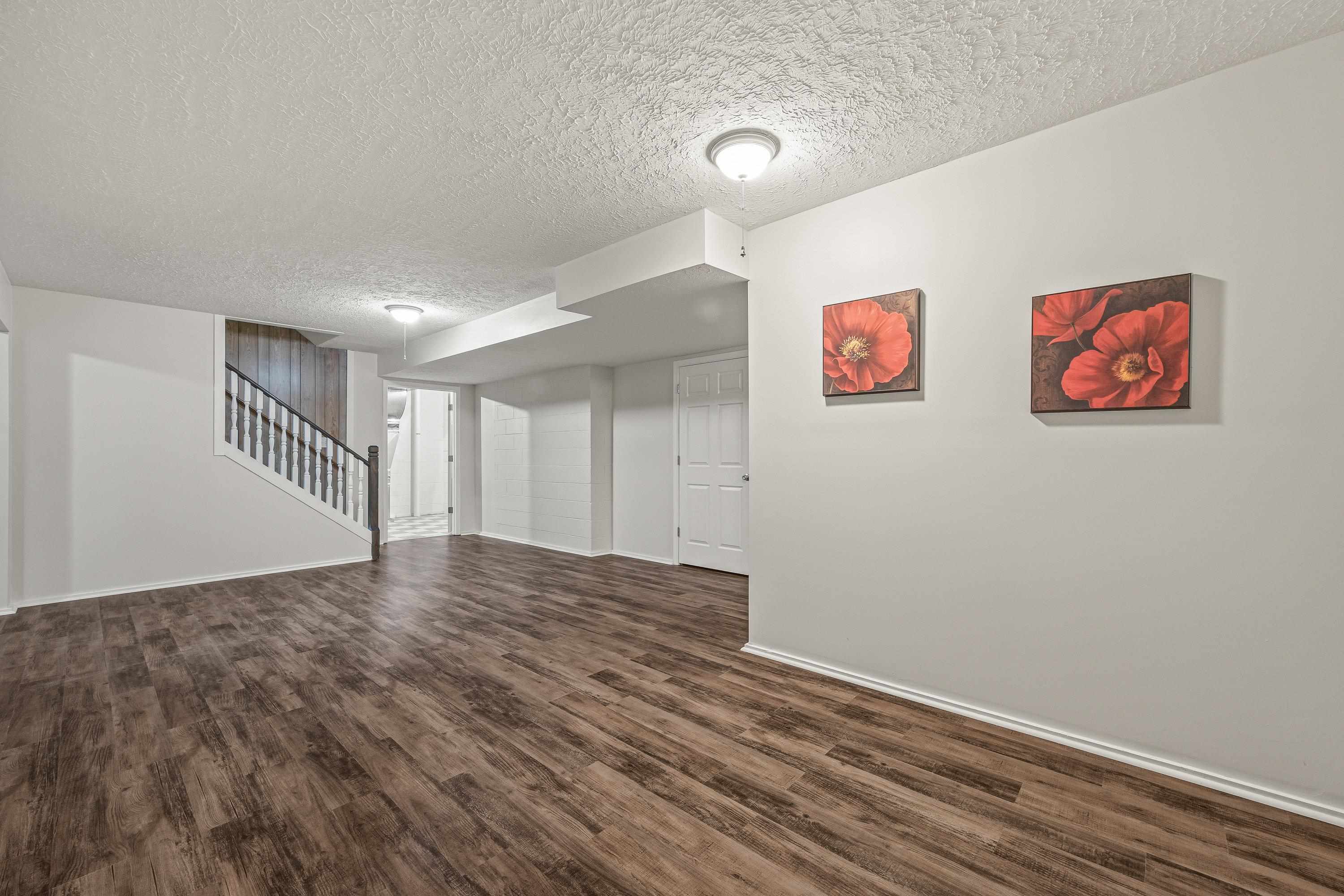 This large space, located at the bottom of the steps to the basement can be used for a varity of purposes including an exercise room, play space, etc.  This room features luxury vinyl plank, recessed lighting, and an attached 1/2 bathroom.