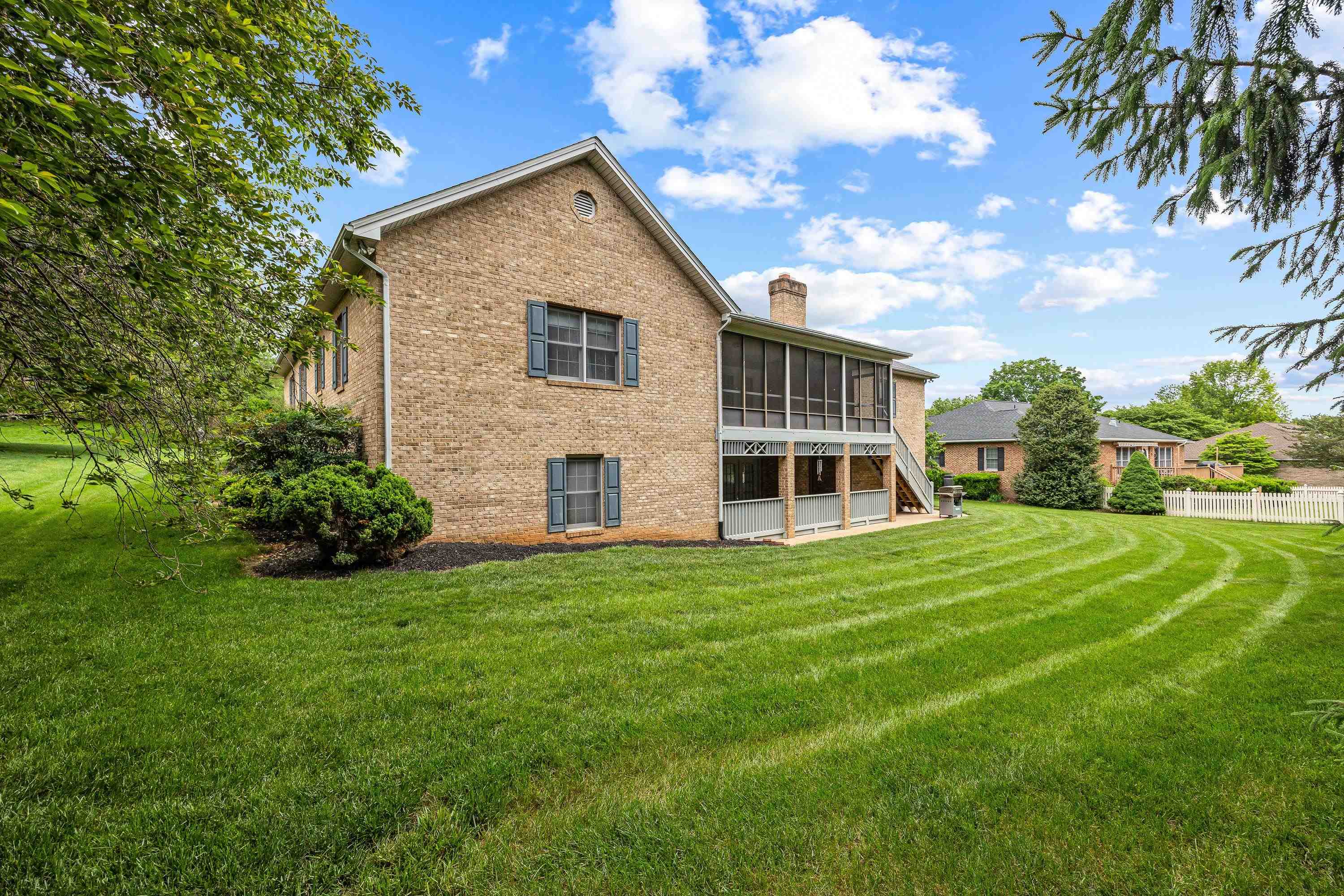 The rear view of the home highlights the mature yard and landscaping surrounding the home.  The large screened-in porch and deck are also highlights of this backyard area.