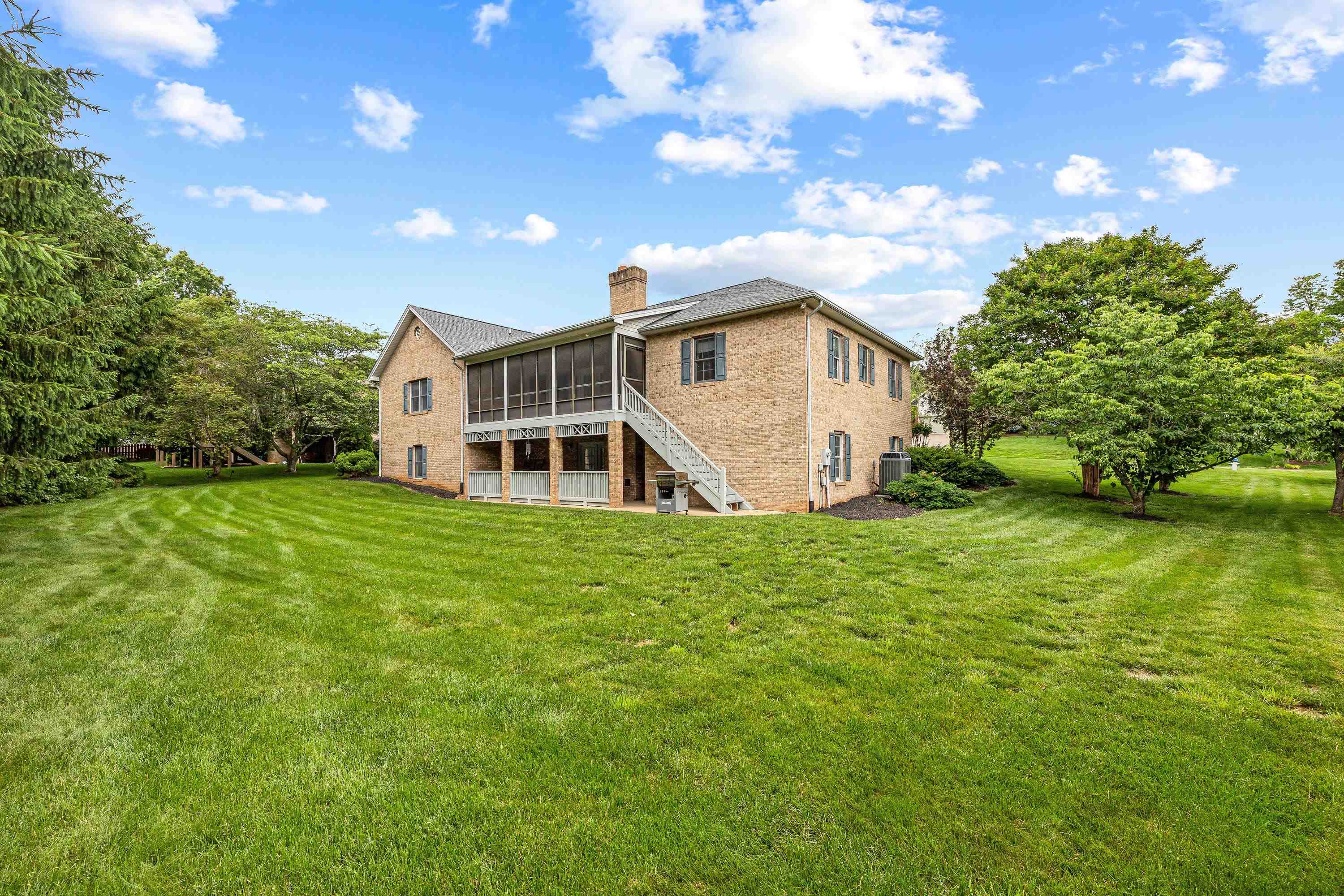 The rear view of the home highlights the mature yard and landscaping surrounding the home.  The large screened-in porch and deck are also highlights of this backyard area.