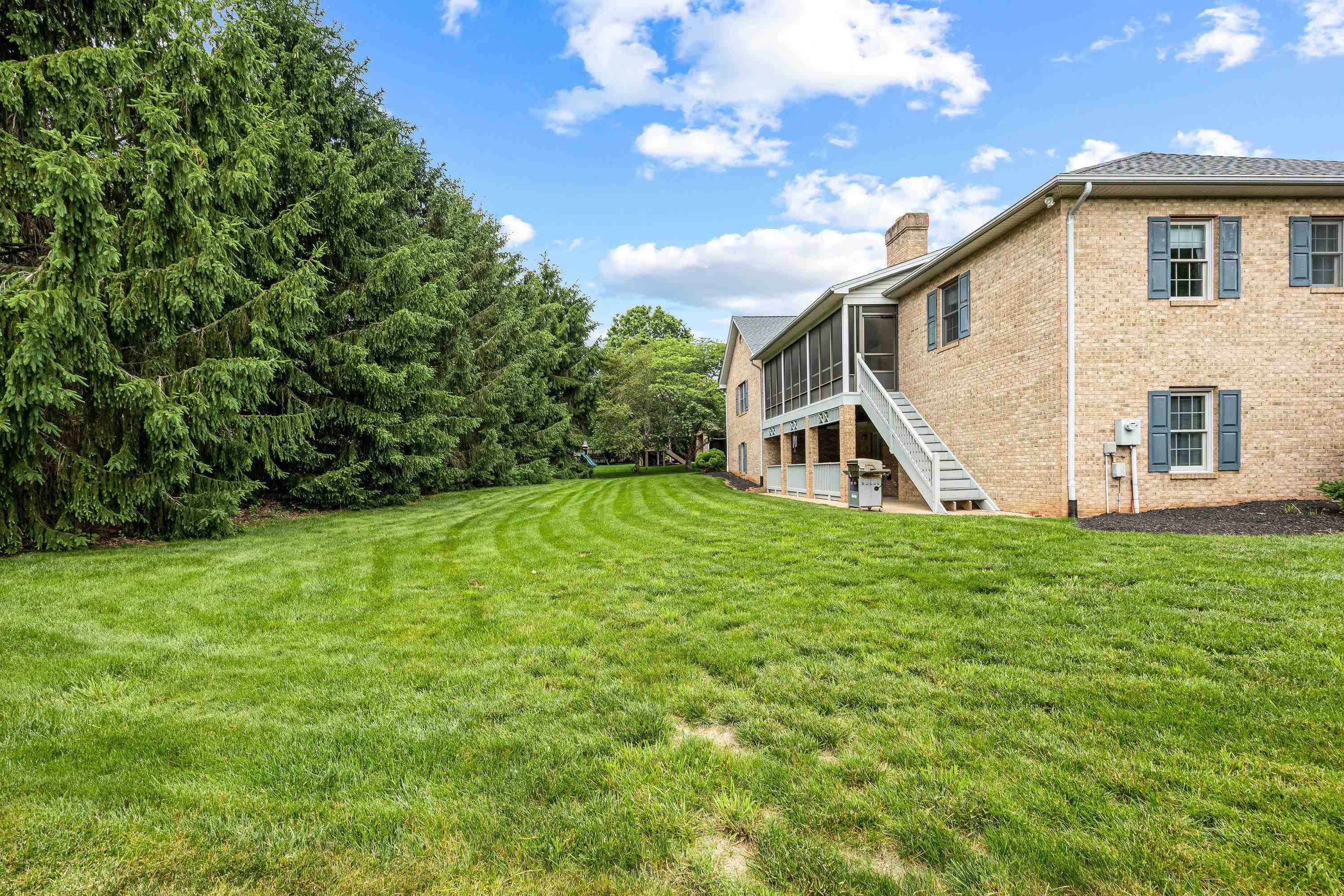 The rear view of the home highlights the mature yard and landscaping surrounding the home.  The large screened-in porch and deck are also highlights of this backyard area.