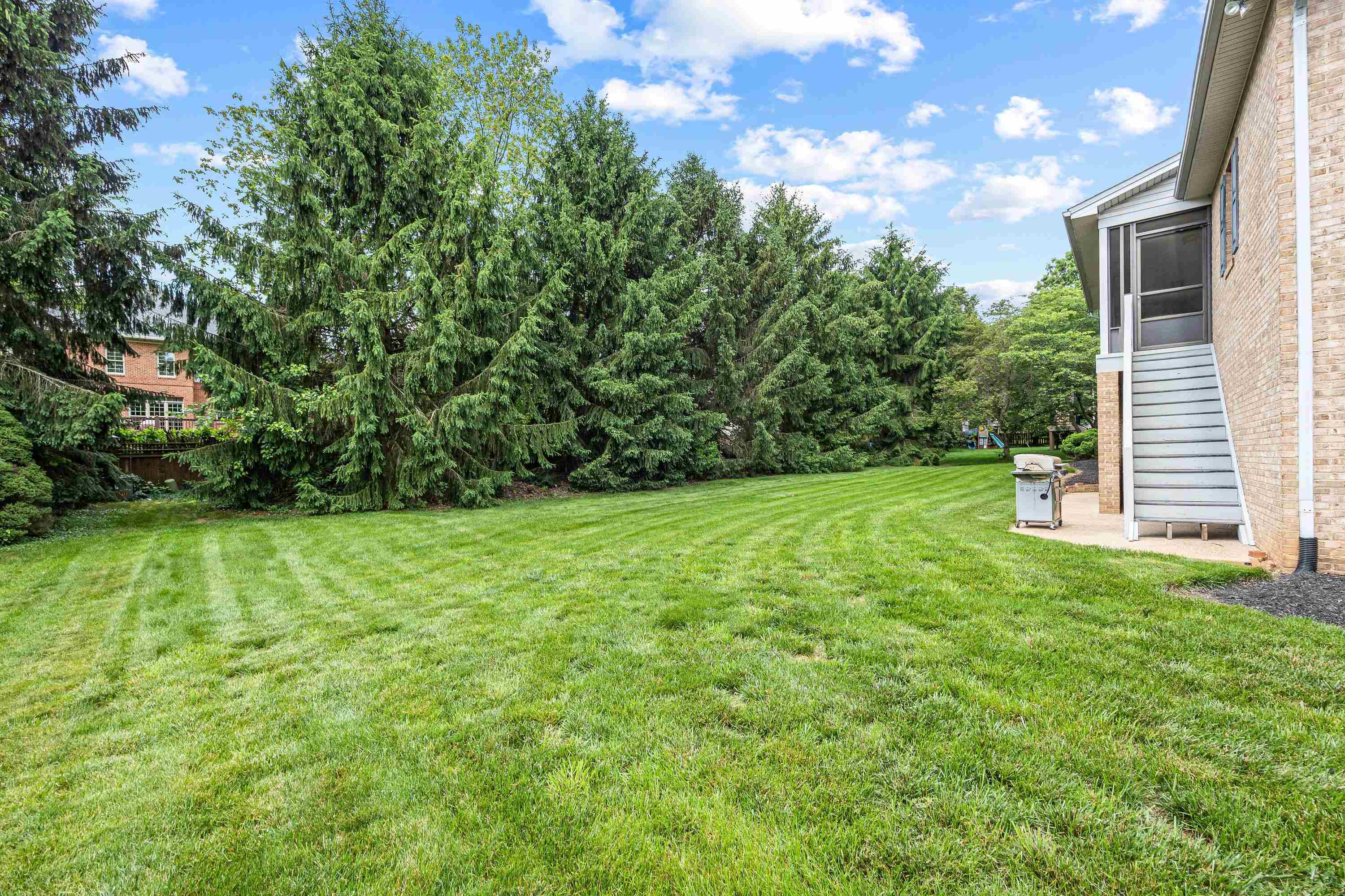 The rear view of the home highlights the mature yard and landscaping surrounding the home.  The large screened-in porch and deck are also highlights of this backyard area.