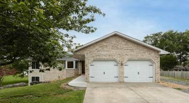 The front view of the home highlights the brick exterior, concrete driveway, two-car garage, new sidewalk, and mature landscaping surrounding the home.
