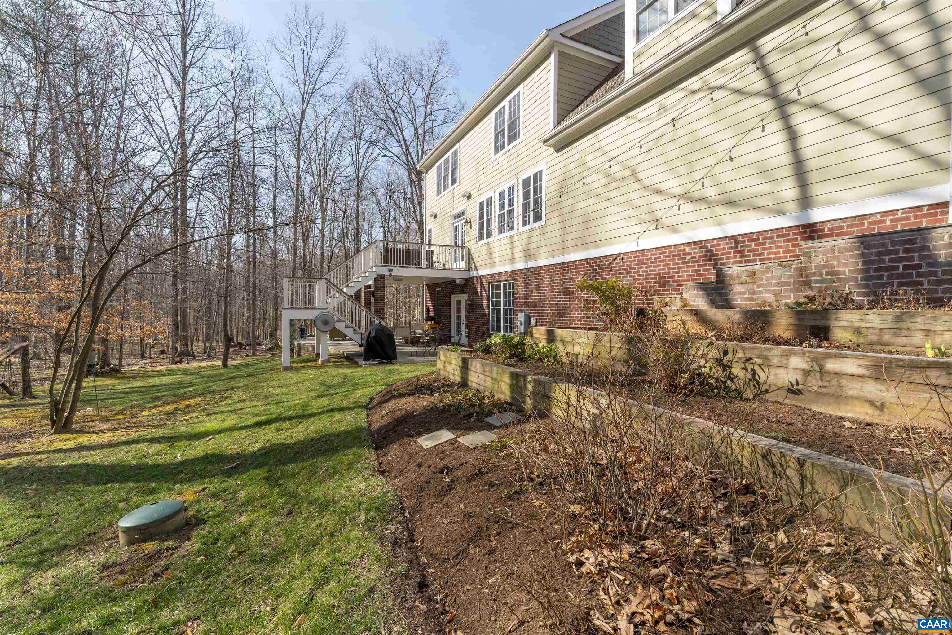 Planting beds at back of garage.  Looking towards deck and patio with fire pit beyond.  Notice strung Edison bulb lights.