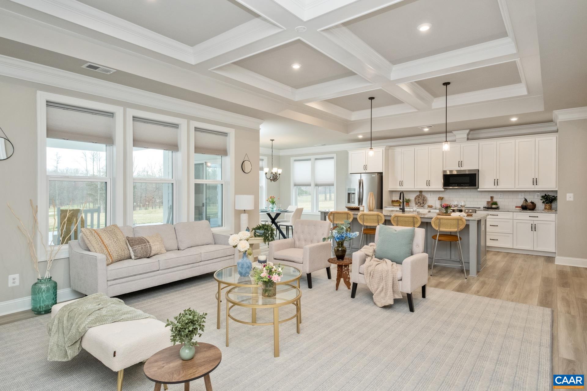 The living room features a raised tray and coffered ceiling, triple windows to allow in plenty of sunlight, and a custom-made rug that conveys.