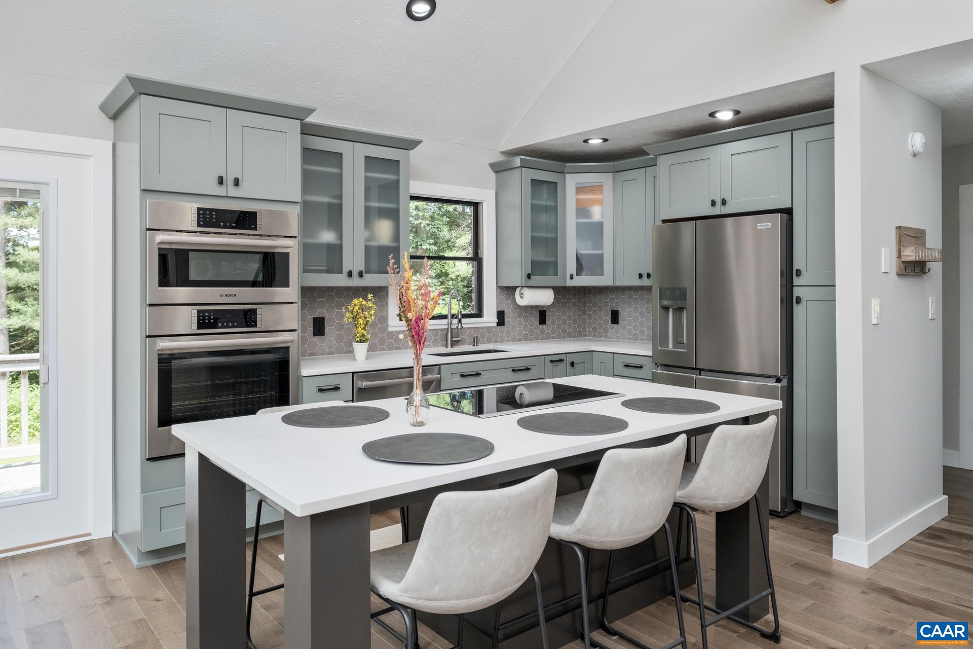 The kitchen has been fully renovated and includes new cabinetry, quartz countertops and sink, a large island with seating, cooktop, and workspace, a backsplash, new high-end appliances, and solid maple floors.
