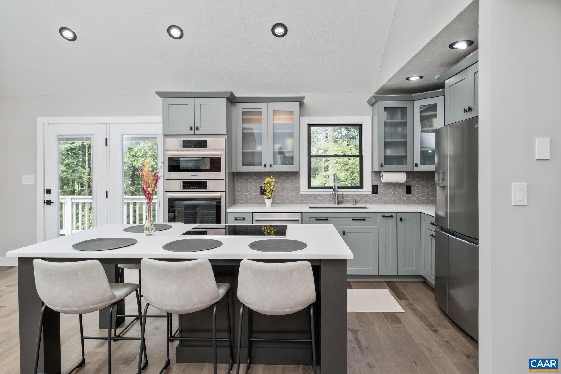 The kitchen has been fully renovated and includes new cabinetry, quartz countertops and sink, a large island with seating, cooktop, and workspace, a backsplash, new high-end appliances, and solid maple floors.
