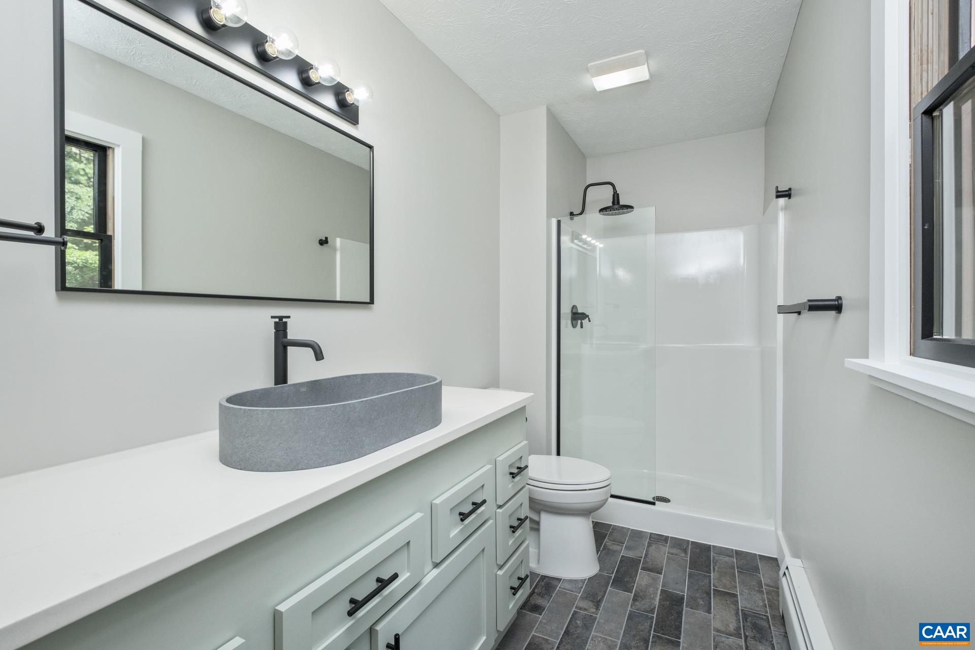 The recently renovated primary bathroom features new fixtures, porcelain tile flooring, shower glass enclosure, quartz countertop, and sink.