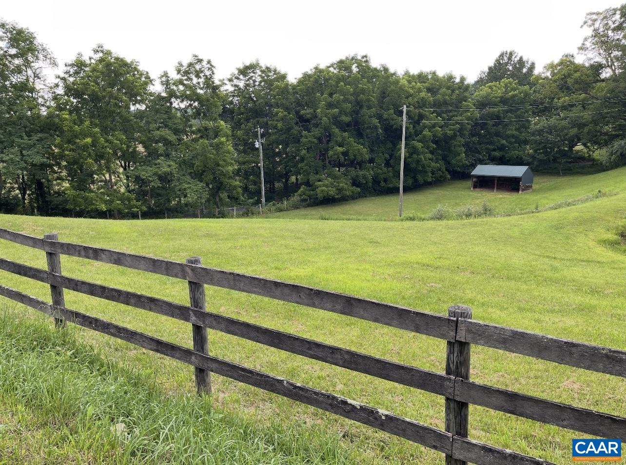 Three boarding fencing along the road with a run-in shed in the distance.