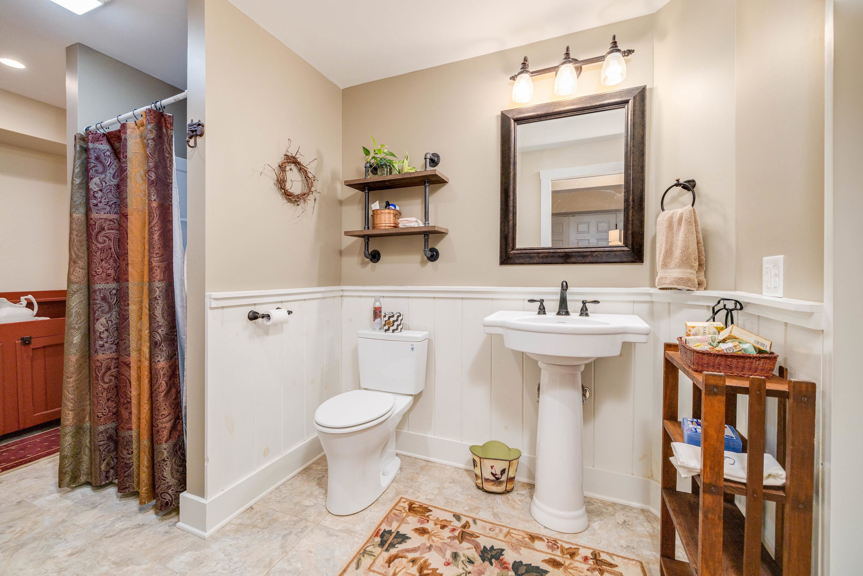 This full bathroom features a pedastal sink, tile shower, and cabinet for additional storage.