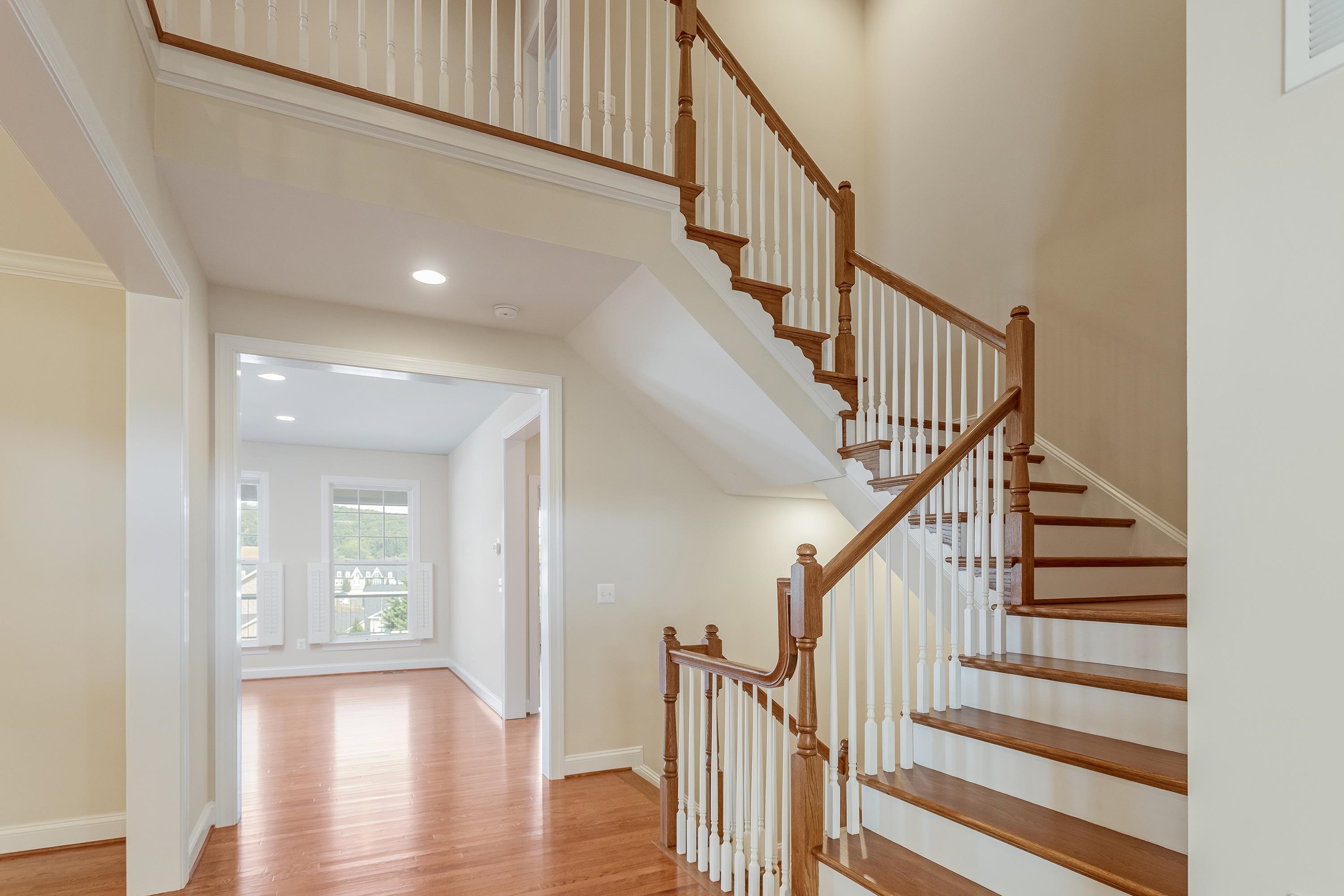 The foyer of the home offers hardwood flooring throughout and a spacious staircase with open railing.