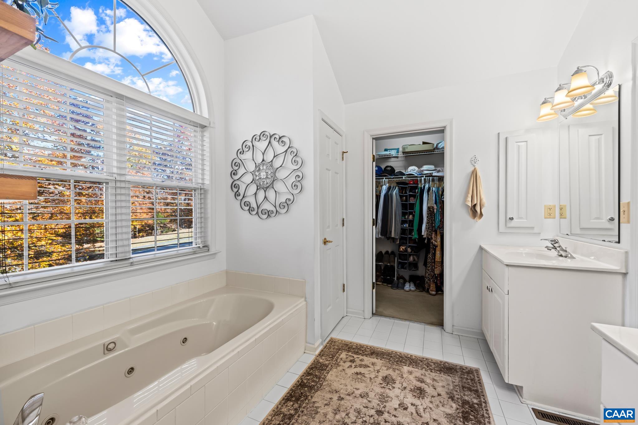 Relax in the jetted tub with a view of the trees. This bright, white primary bathroom features dual vanities, an elegant metal wall accent, and a walk-in closet for all your storage needs. Relax in the jetted tub with a view of the trees. This bright, white primary bathroom features dual vanities, an elegant metal wall accent, and a walk-in closet for all your storage needs.