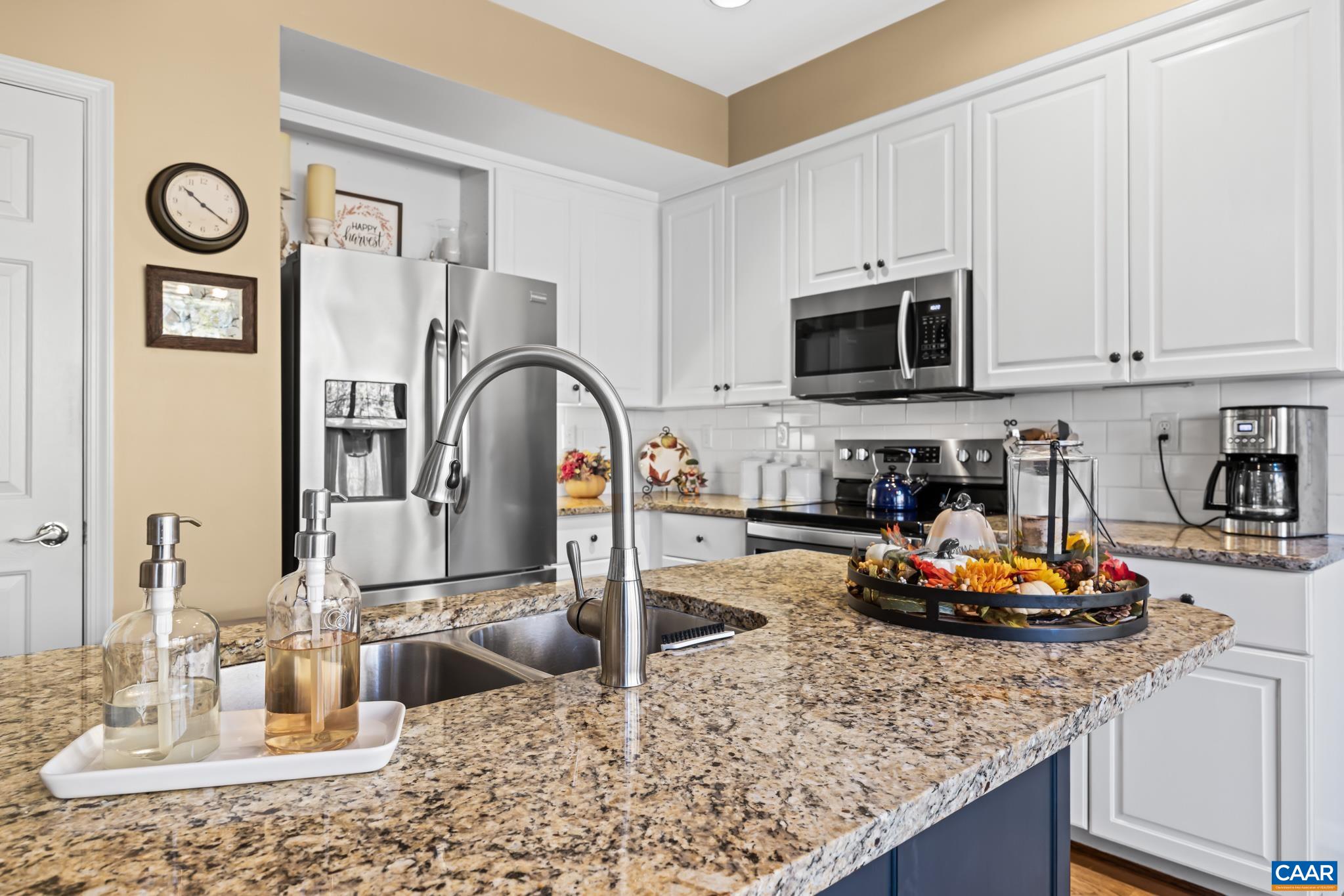 Enjoy cooking in this bright, modern kitchen featuring white shaker cabinets, a subway tile backsplash, and stainless steel appliances, including a microwave, range, and refrigerator. The granite-topped island with a double sink provides ample workspace. Enjoy cooking in this bright, modern kitchen featuring white shaker cabinets, a subway tile backsplash, and stainless steel appliances, including a microwave, range, and refrigerator. The granite-topped island with a double sink provides ample workspace.