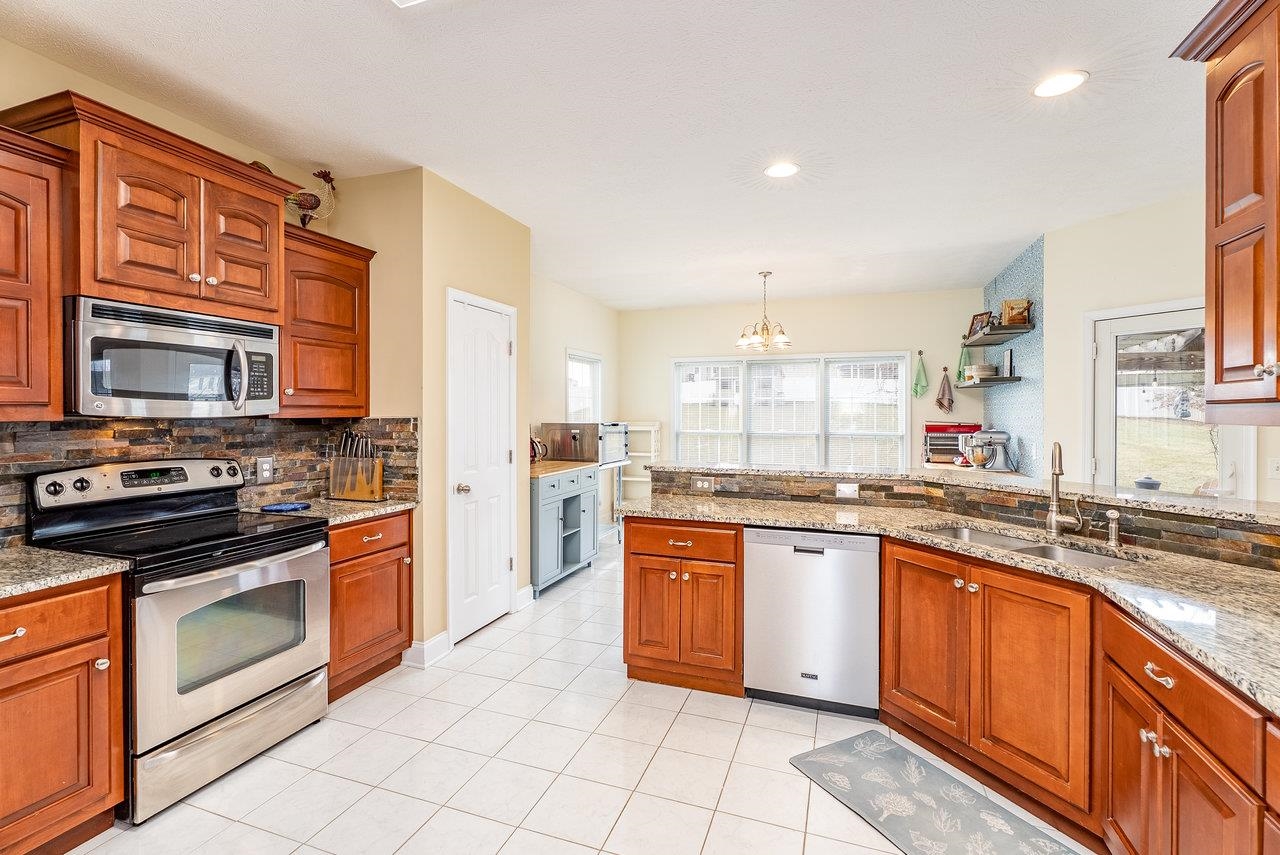 Features: Tile floors paired with rich wood cabinetry, granite countertops, a stylish tile backsplash, and sleek stainless steel appliances.