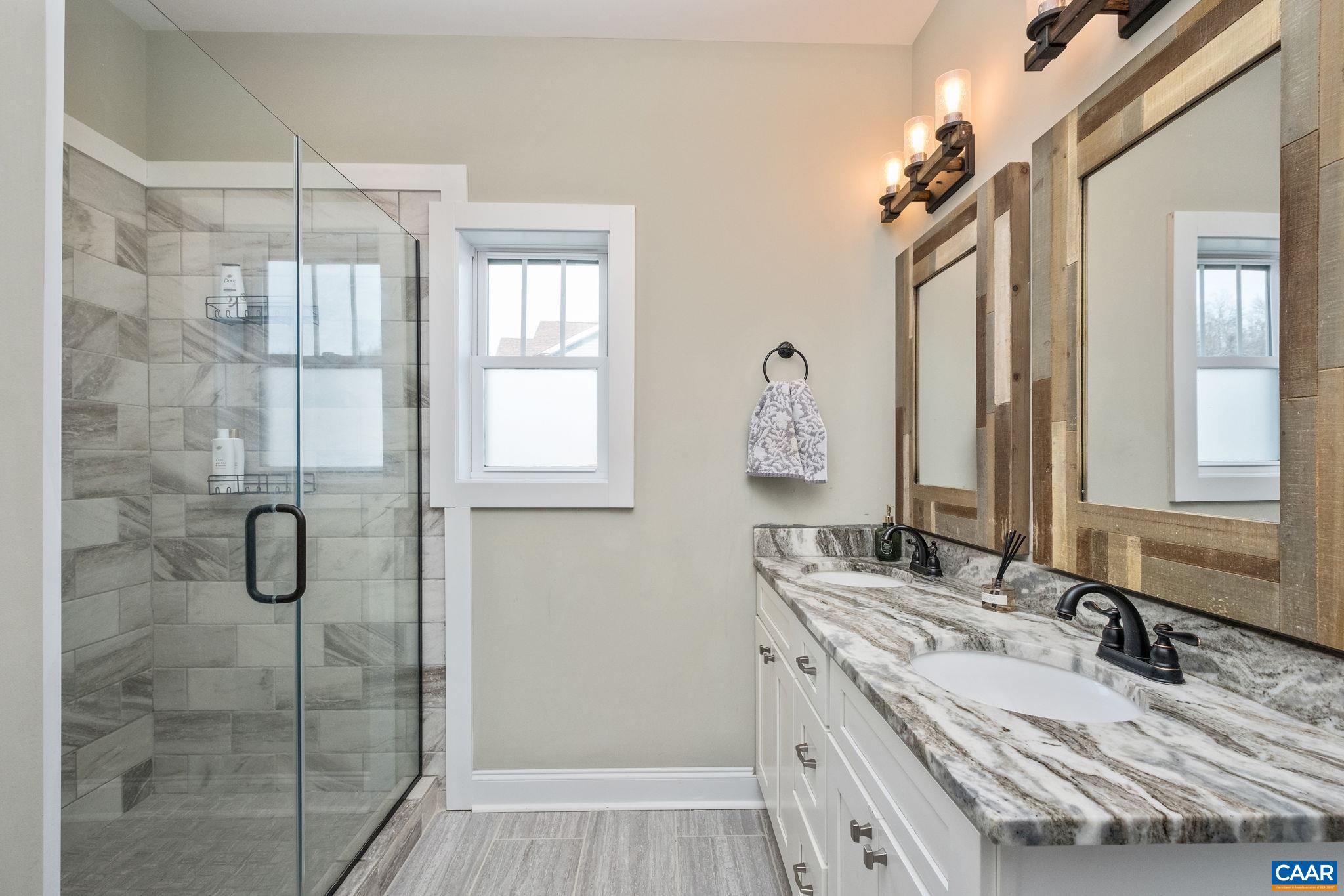 Primary bathroom features porcelain tile flooring, dual vanities, tiled shower, and walk-in closet.