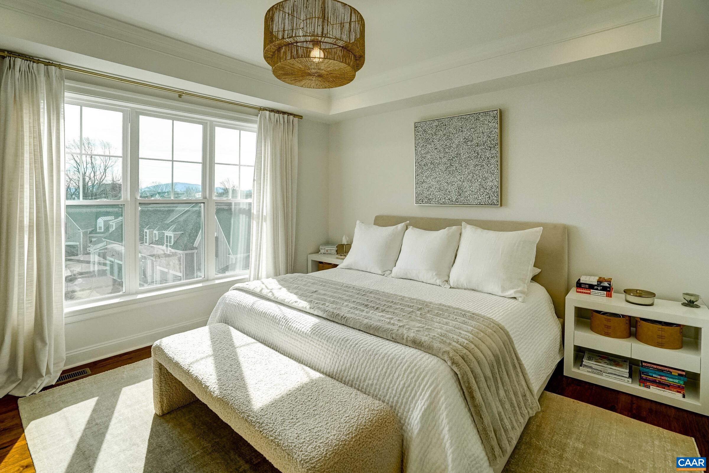 Light-filled primary bedroom with modern custom lighting, tray ceiling and two closets.