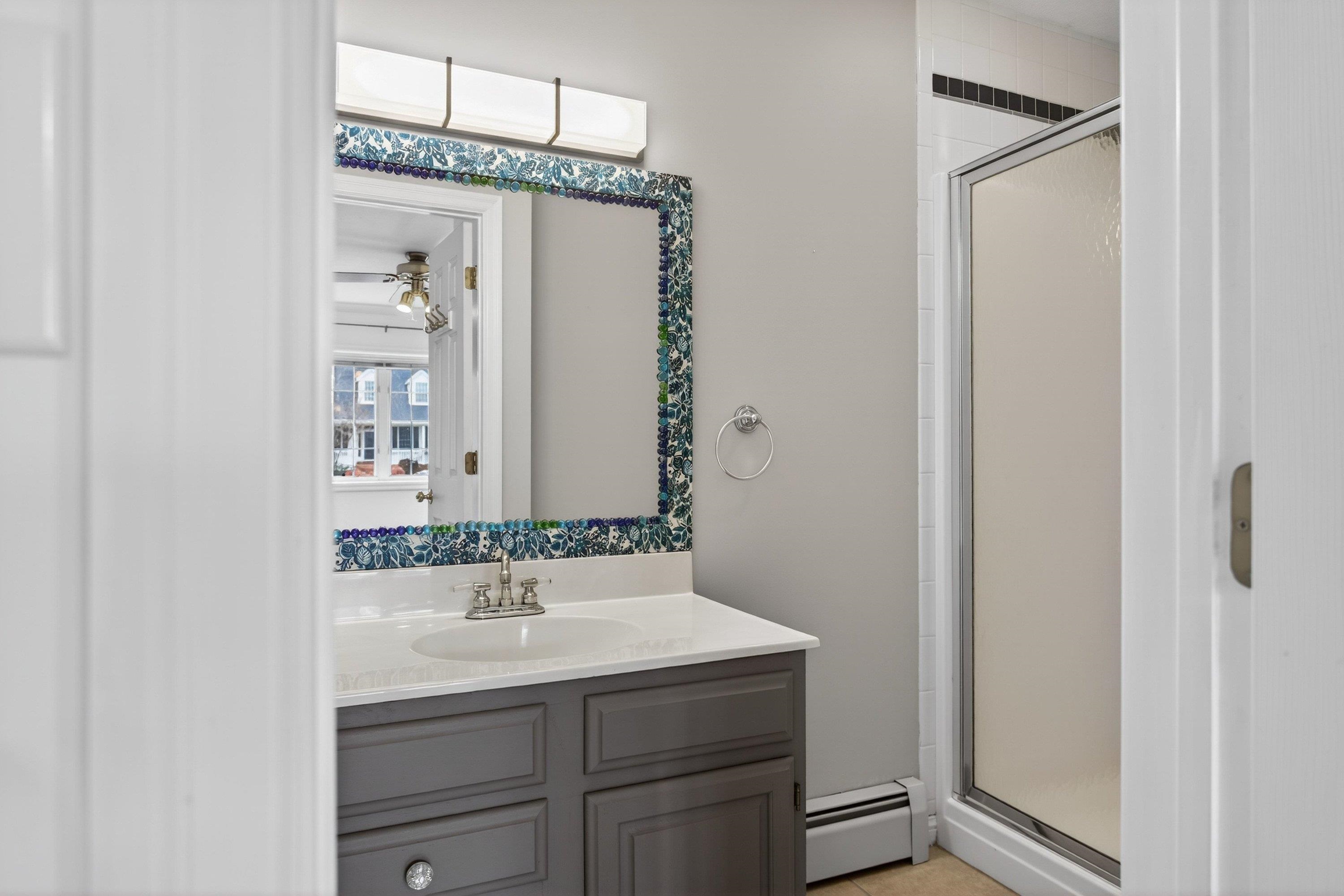 This full bathroom offers a vanity with storage cabinetry, updated light fixture, walk-in shower space, and tile flooring throughout.