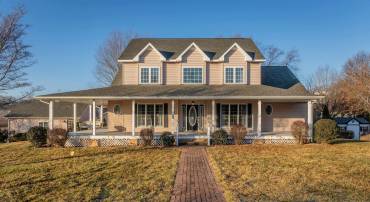 The front view of the home highlights the large wrap-around porch of the home, detached garage, large level yard of the home, and much more!