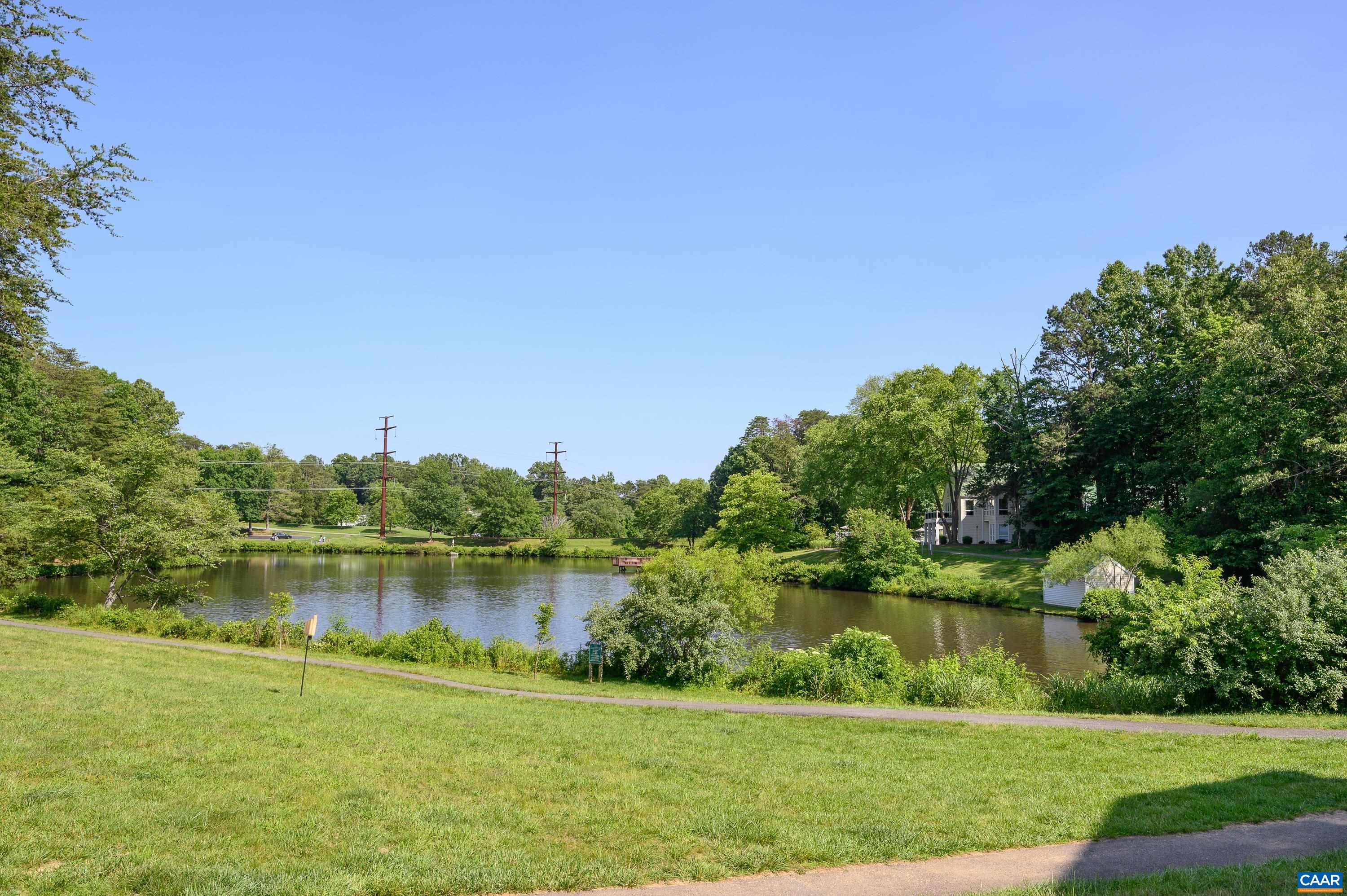 Scenic community pond surrounded by mature trees and walking paths, offering peaceful views and outdoor enjoyment just steps away.