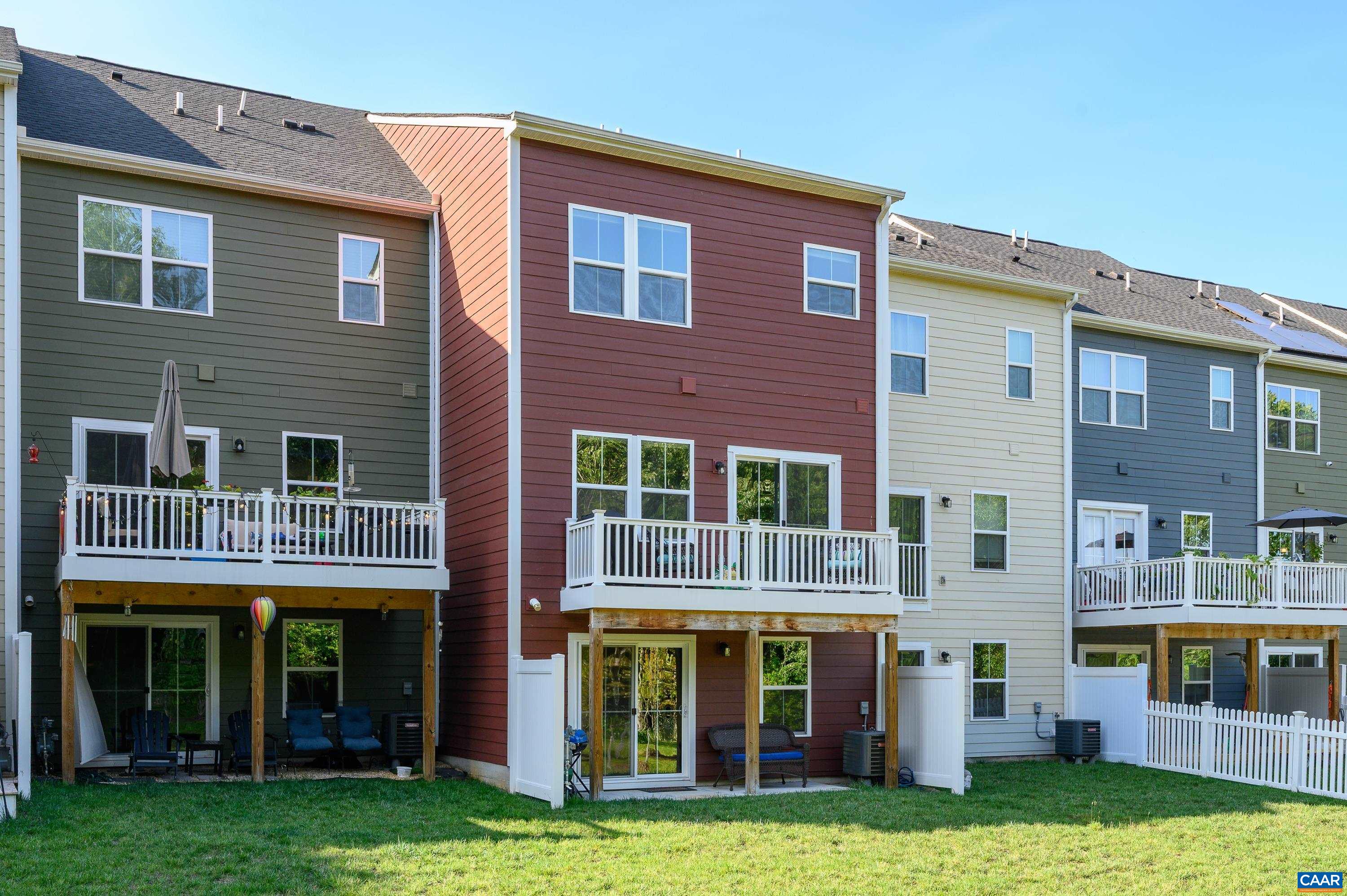 Rear elevation featuring private deck, lower-level patio, and open green space. Ideal for relaxing or entertaining outdoors.