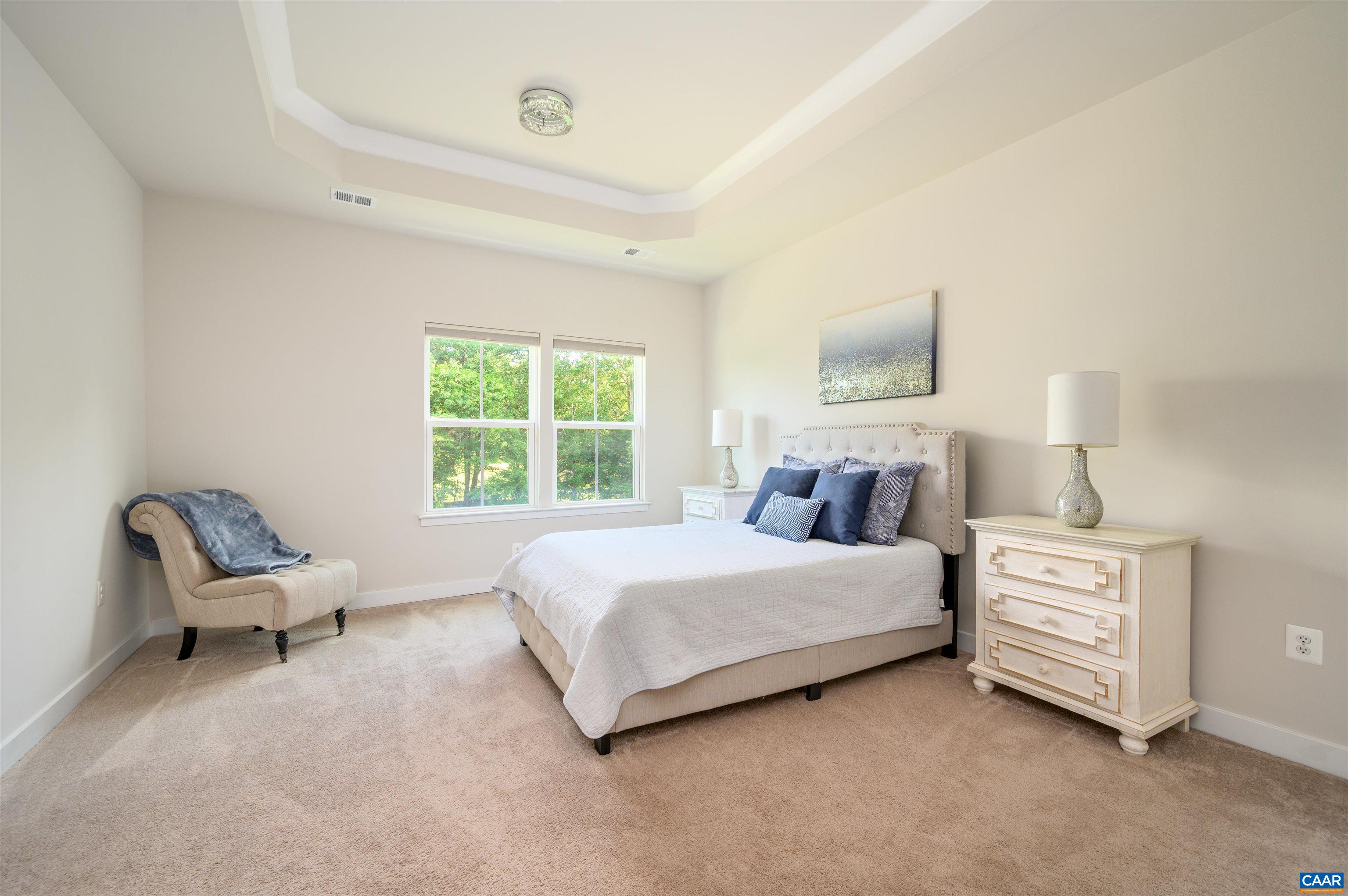 Spacious primary bedroom retreat with tray ceiling, large windows overlooking green space, room for additional seating, and private ensuite bathroom.