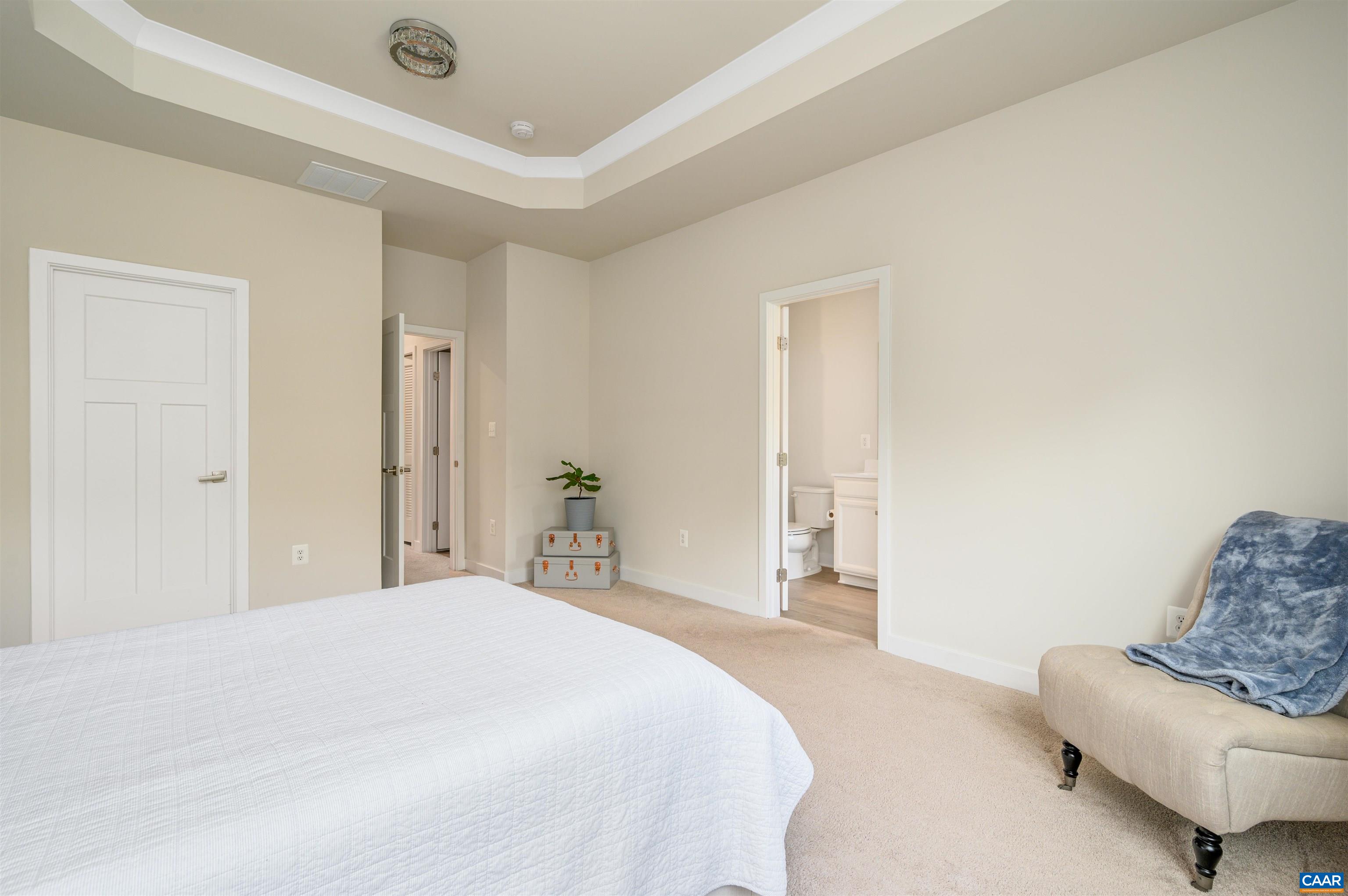 Spacious primary bedroom retreat with tray ceiling, large windows overlooking green space, room for additional seating, and private ensuite bathroom.