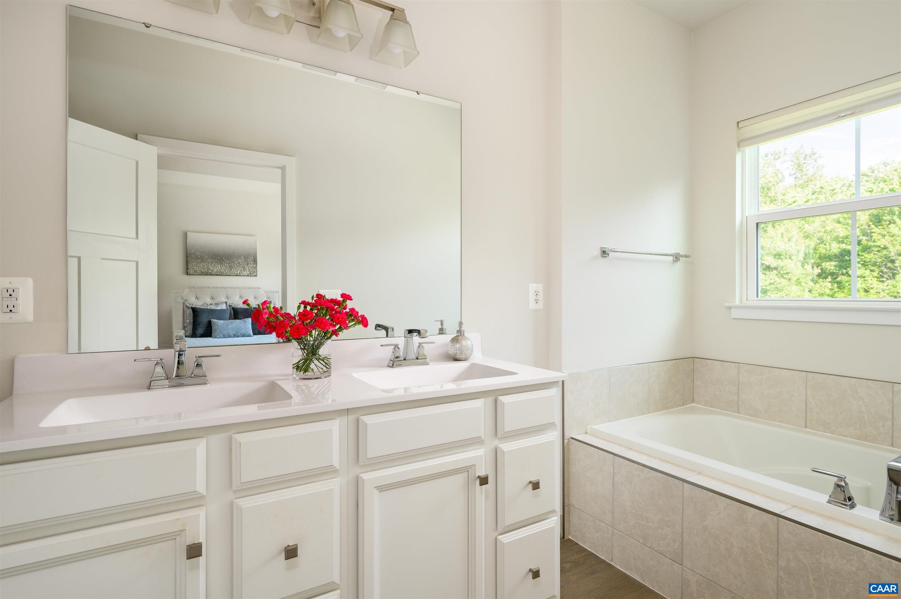 Bright and spacious primary bath featuring dual vanities with ample storage, a large soaking tub with tile surround, and an expansive mirror for added light and openness.