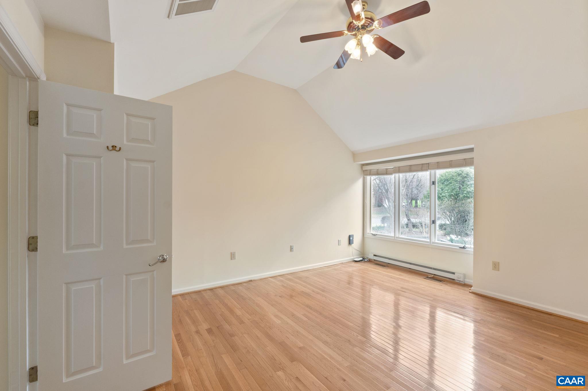 Primary suite features vaulted ceiling and hardwood flooring