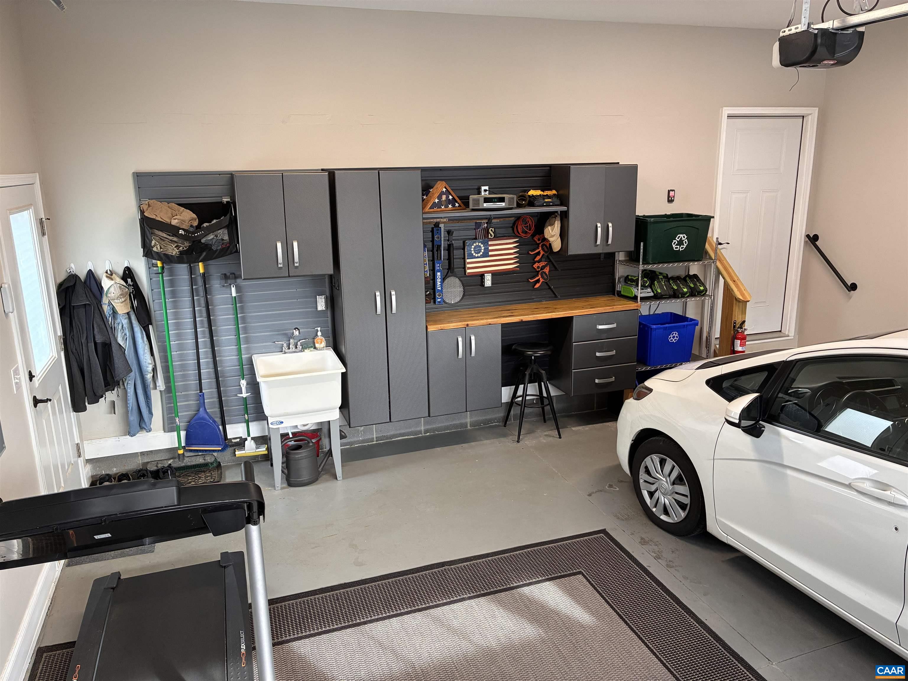 The garage features custom cabinetry, a workbench with additional outlets, a utility sink, and a side door that provides easy access to the custom built shed. The garage features custom cabinetry, a workbench with additional outlets, a utility sink, and a side door that provides easy access to the custom built shed.
