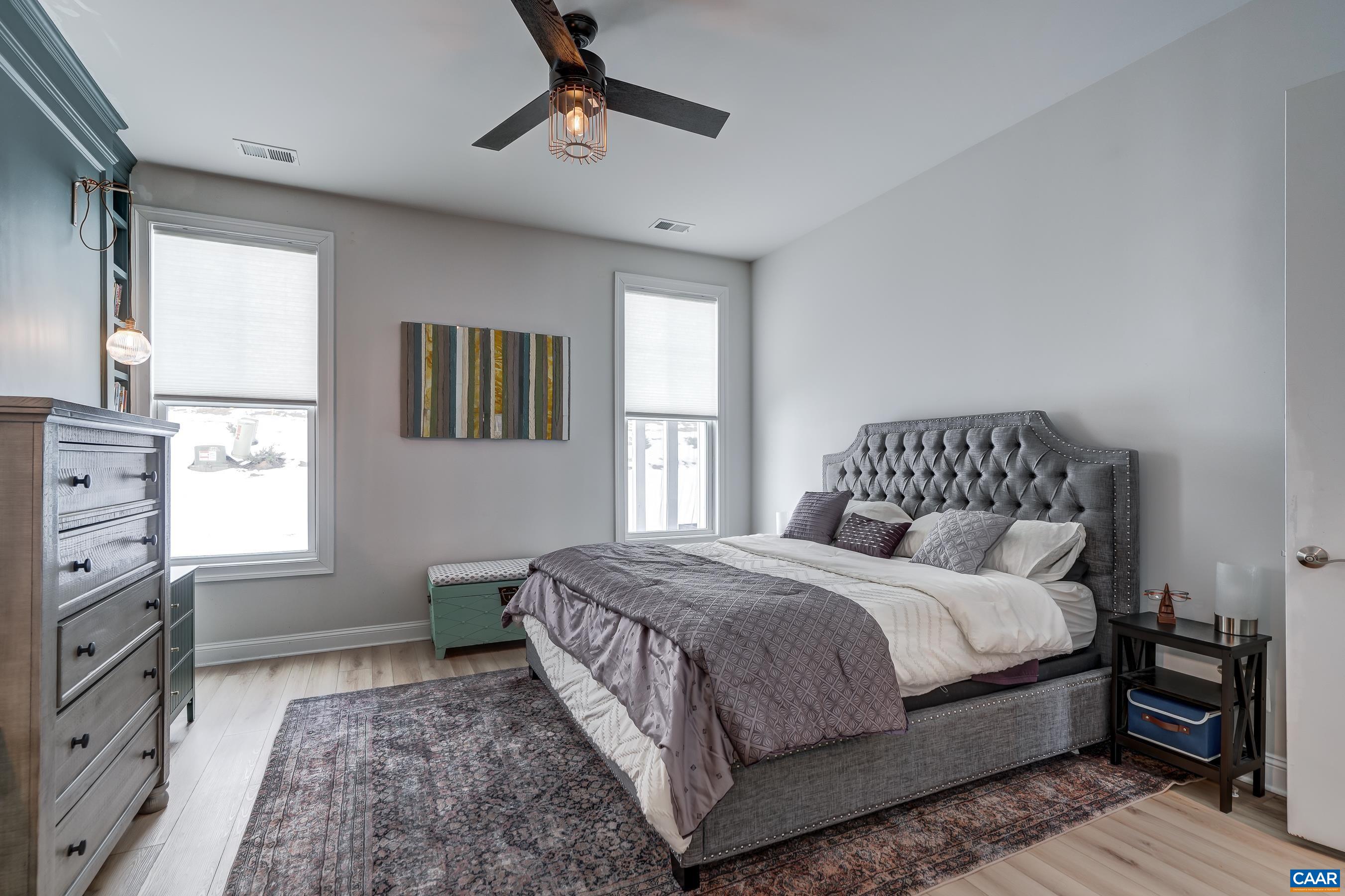Main level primary suite features ceiling fan, light-filtering window treatments and custom built-ins.