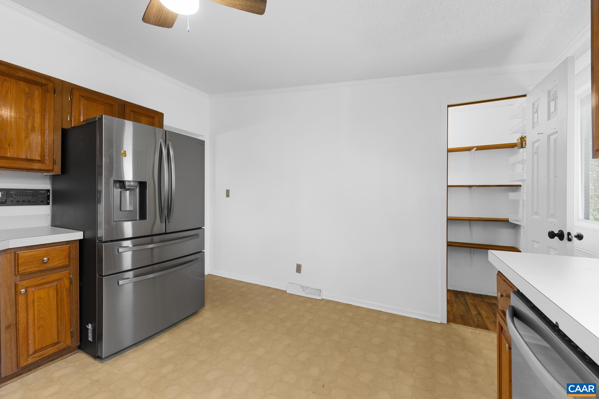 Enjoy a spacious kitchen with a modern stainless steel refrigerator and ample white countertop space. The area features wood cabinets, easy-to-clean flooring, and a walk-in pantry with shelving. Enjoy a spacious kitchen with a modern stainless steel refrigerator and ample white countertop space. The area features wood cabinets, easy-to-clean flooring, and a walk-in pantry with shelving.