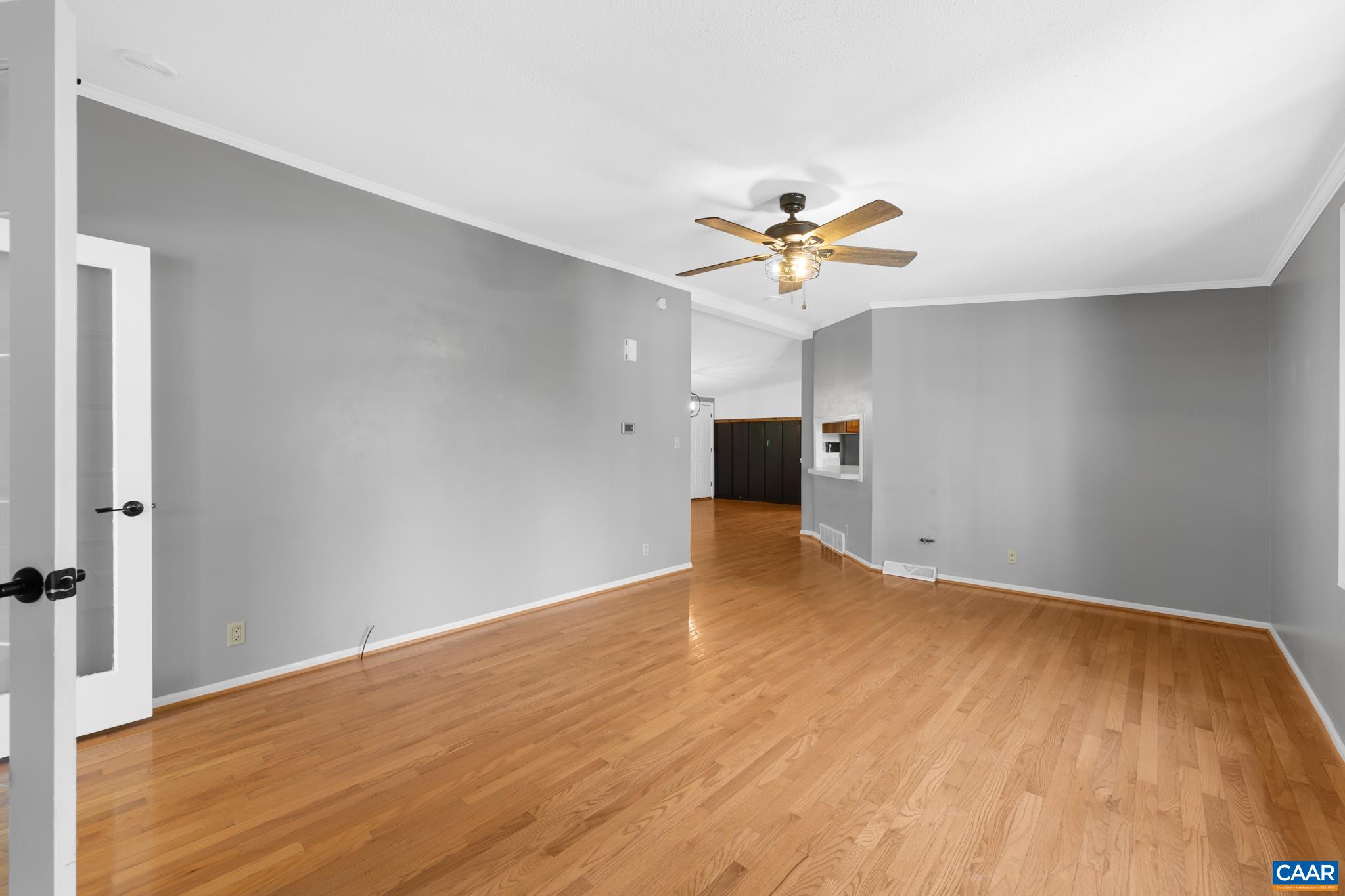 Imagine life in this bright, inviting space! Gray walls and beautiful hardwood floors create a welcoming atmosphere. A peek past the corner shows a convenient pass-through window, connecting to the kitchen. Perfect for entertaining! Imagine life in this bright, inviting space! Gray walls and beautiful hardwood floors create a welcoming atmosphere. A peek past the corner shows a convenient pass-through window, connecting to the kitchen. Perfect for entertaining!
