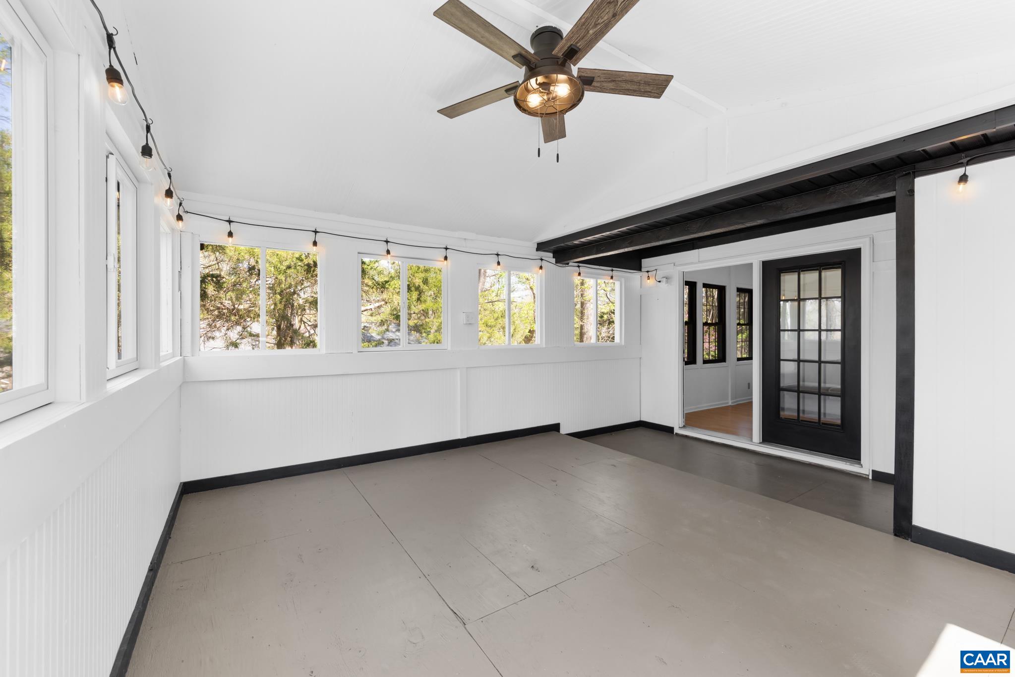 Bright, spacious sunroom with ample natural light, painted white walls, and a ceiling fan. It leads directly to office indoor space via a black-framed French door. Perfect spot for relaxation or an extension of your home office! Bright, spacious sunroom with ample natural light, painted white walls, and a ceiling fan. It leads directly to office indoor space via a black-framed French door. Perfect spot for relaxation or an extension of your home office!