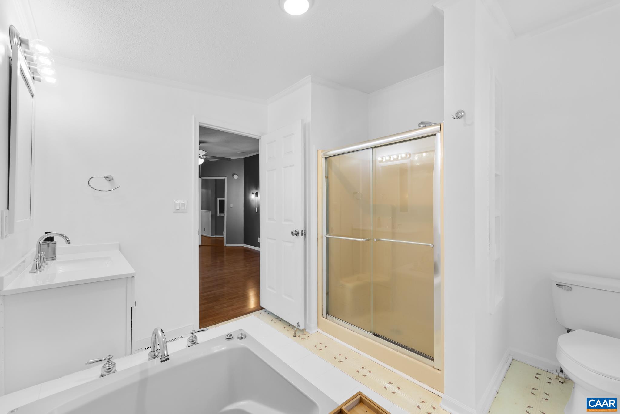 Bright, white bathroom with a deep soaking tub and a separate glass-enclosed shower, offering a clean and spa-like retreat. Hardwood floors peek through the doorway, hinting at the home's flow. Bright, white bathroom with a deep soaking tub and a separate glass-enclosed shower, offering a clean and spa-like retreat. Hardwood floors peek through the doorway, hinting at the home's flow.