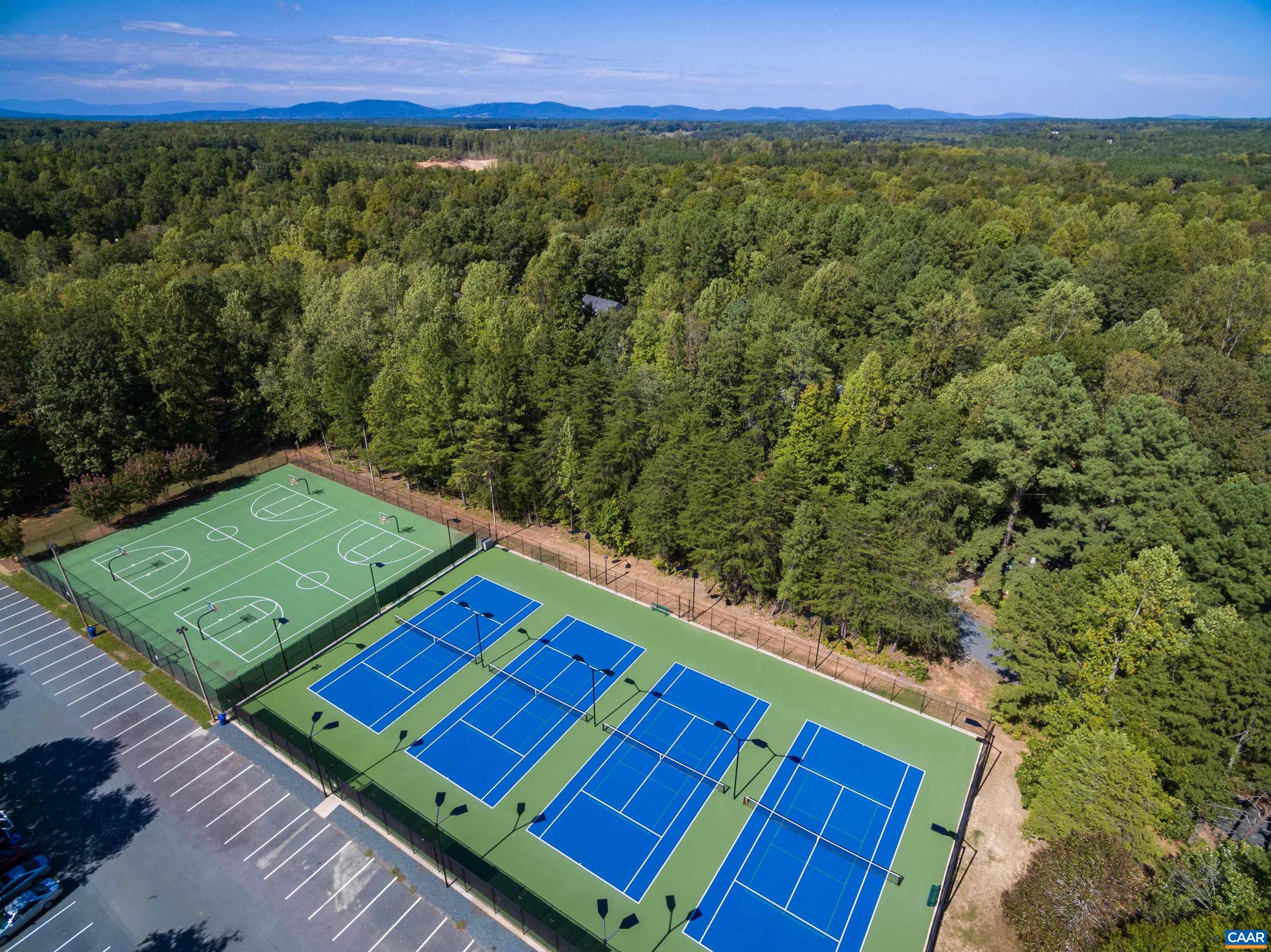 Enjoy active living! The image shows four bright blue tennis courts and two green basketball courts, right next to a spacious parking lot. Surrounded by lush, green trees and mountain views. Enjoy active living! The image shows four bright blue tennis courts and two green basketball courts, right next to a spacious parking lot. Surrounded by lush, green trees and mountain views.