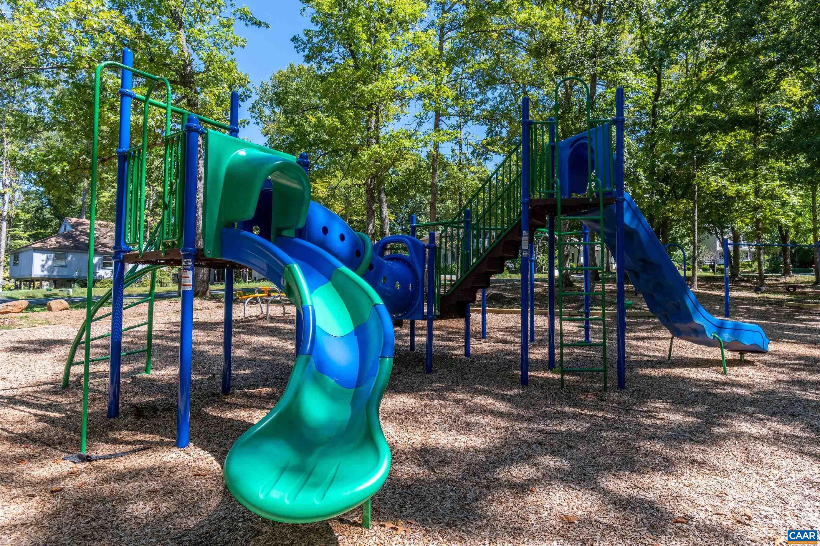 Discover fun! The image shows a vibrant playground nestled among trees, featuring blue and green slides and climbing structures on a wood chip base. Bring the kids to enjoy hours of outdoor play and adventure in this beautiful setting. Discover fun! The image shows a vibrant playground nestled among trees, featuring blue and green slides and climbing structures on a wood chip base. Bring the kids to enjoy hours of outdoor play and adventure in this beautiful setting.