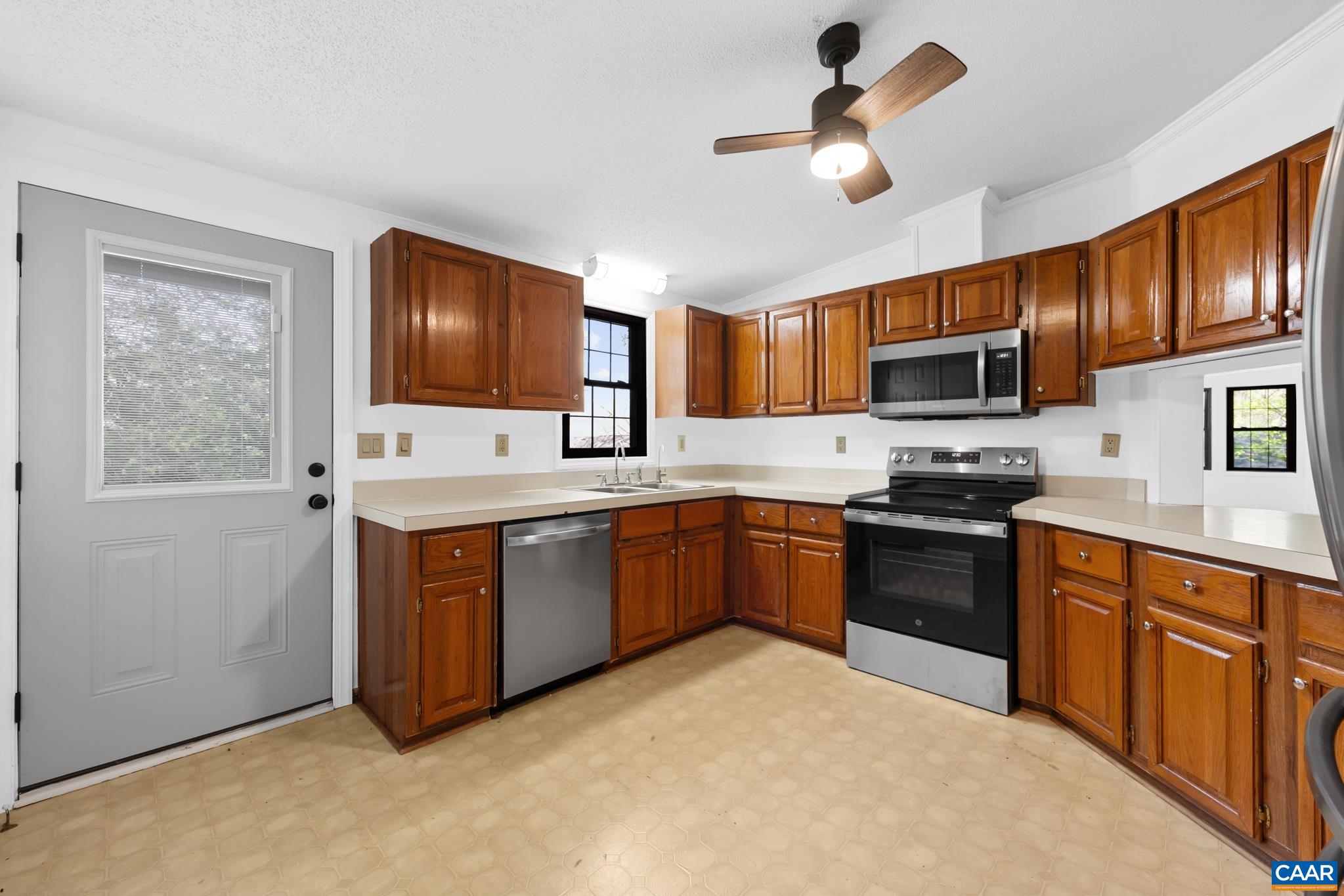 Bright kitchen with warm wood cabinets, ample counter space, and stainless steel appliances, including a microwave, dishwasher, and range. Features a ceiling fan and outdoor access. Bright kitchen with warm wood cabinets, ample counter space, and stainless steel appliances, including a microwave, dishwasher, and range. Features a ceiling fan and outdoor access.