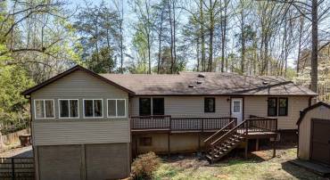 The rear of the home shows more of what the house has to offer. Welcome home! This charming one-level property features a spacious rear deck, fenced backyard, and a private driveway. Inside, enjoy a sunroom, flexible floor plan, and workshop space.