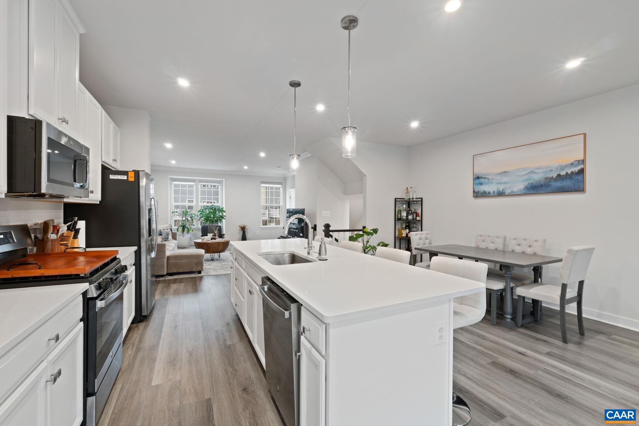 Modern kitchen featuring large center island with seating, stainless steel appliances, white cabinetry, and open flow to dining and living areas. Modern kitchen featuring large center island with seating, stainless steel appliances, white cabinetry, and open flow to dining and living areas.