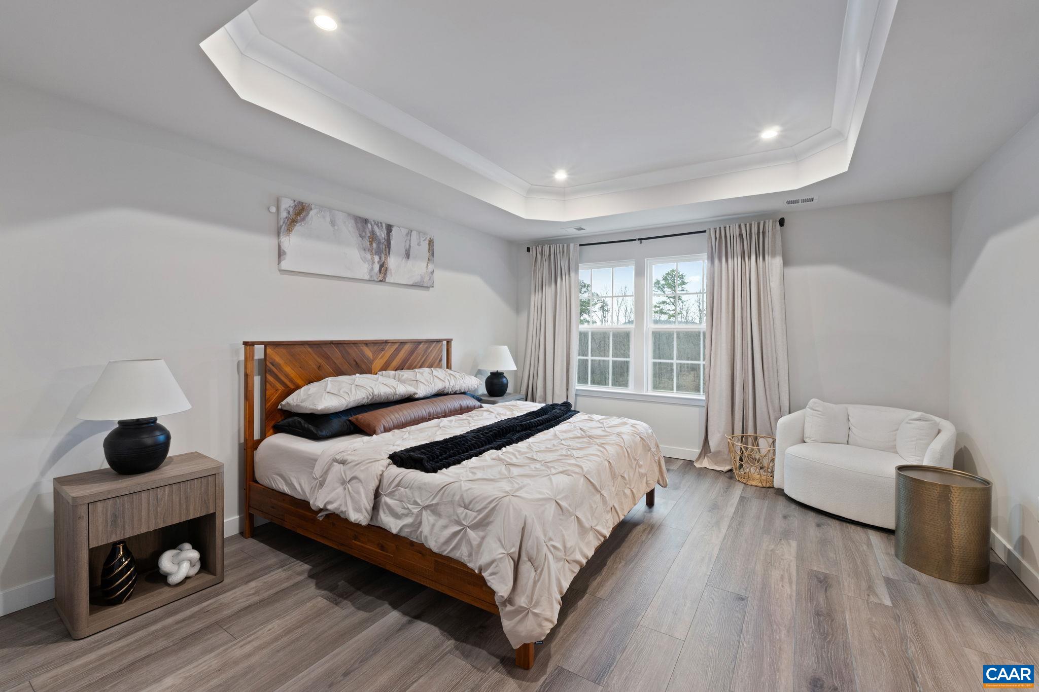 Spacious primary bedroom featuring tray ceiling detail, large windows for natural light, and ample space for a sitting area—creating a comfortable and inviting retreat. Spacious primary bedroom featuring tray ceiling detail, large windows for natural light, and ample space for a sitting area—creating a comfortable and inviting retreat.